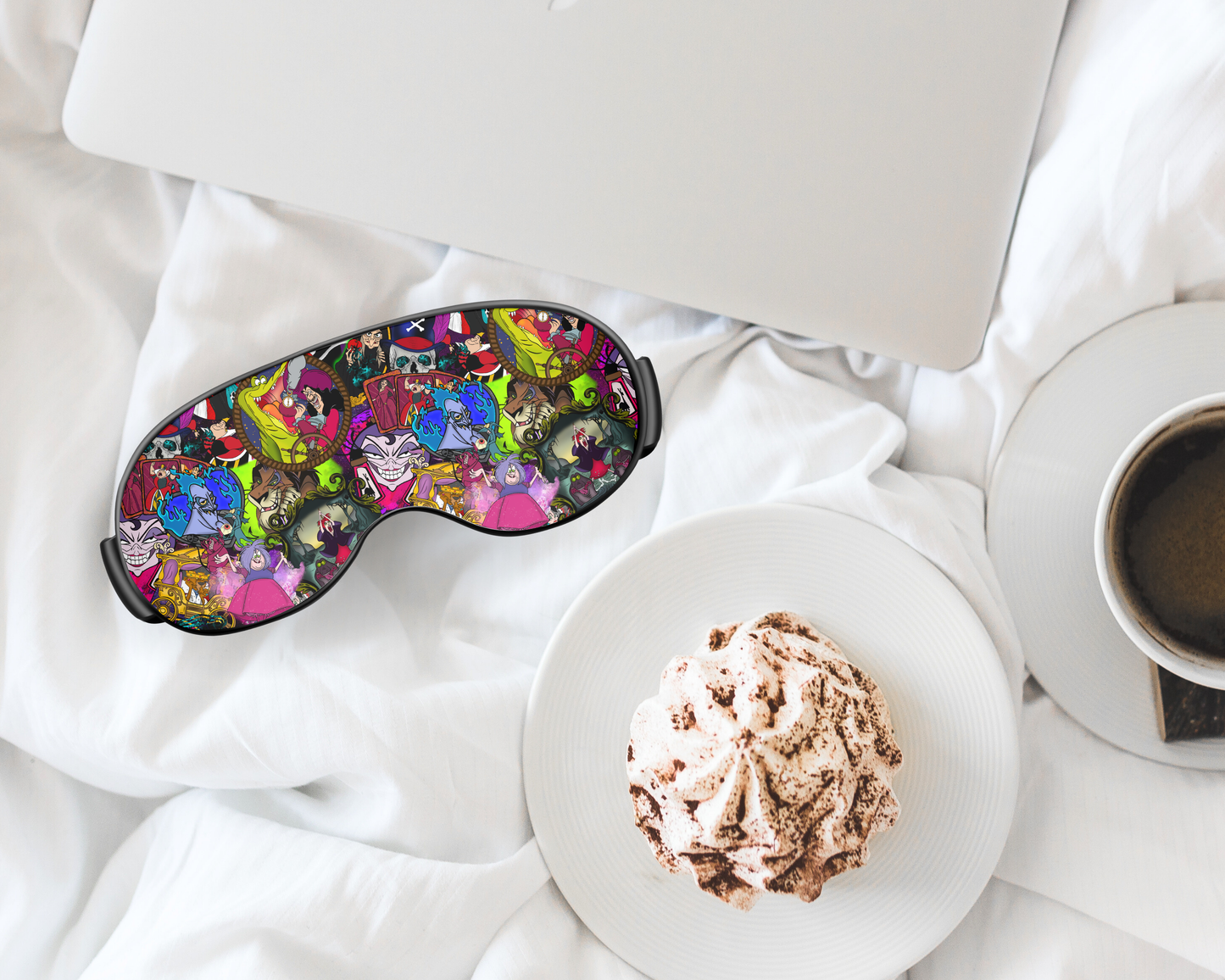 Colorful sleep mask with cartoon characters on a white surface next to a cup of coffee and dessert.