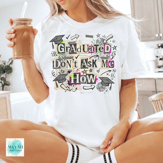 Person wearing a white t-shirt with graduation-themed text, sitting in a kitchen.