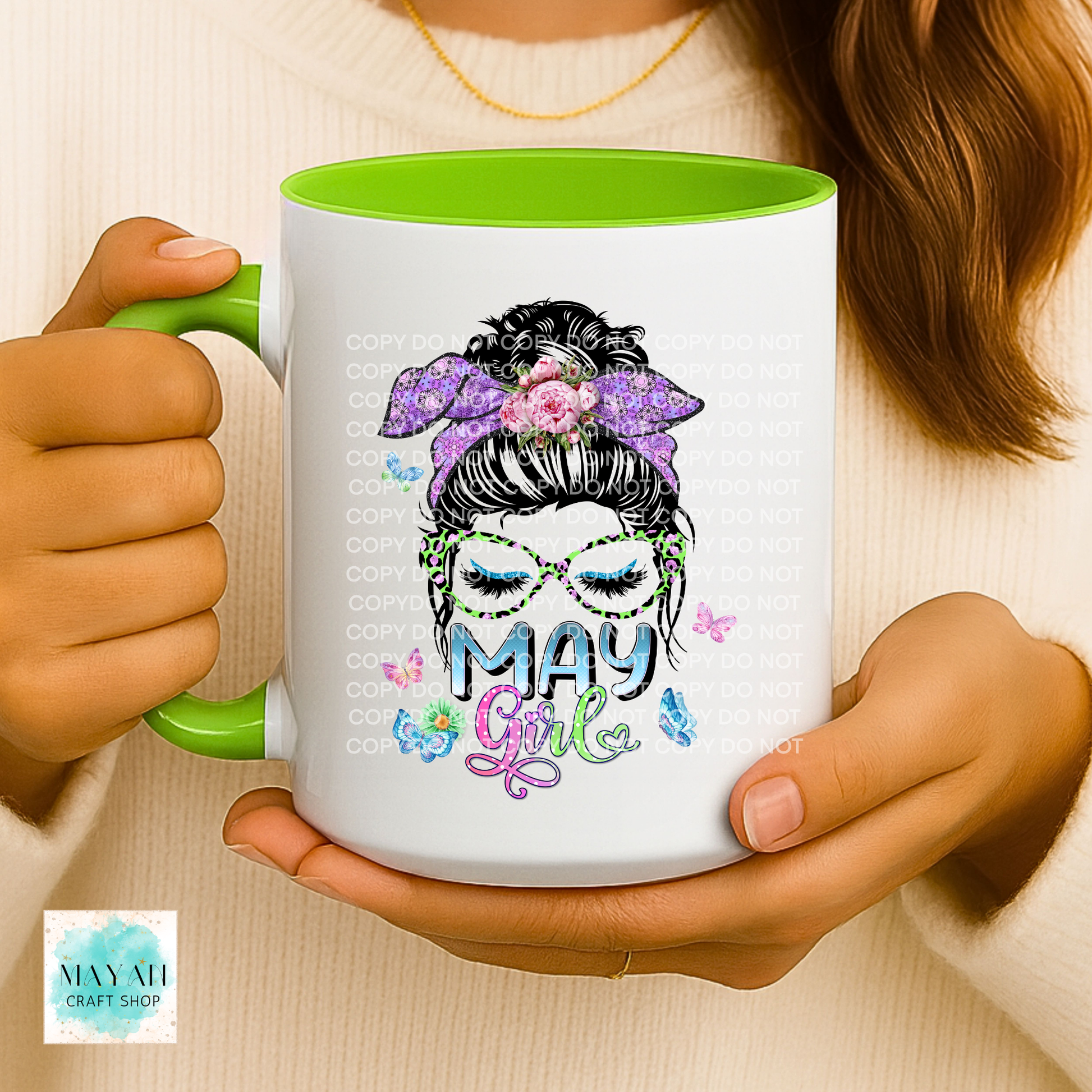 Person holding a mug with a colorful design and 'May Girl' text, wearing a beige sweater.