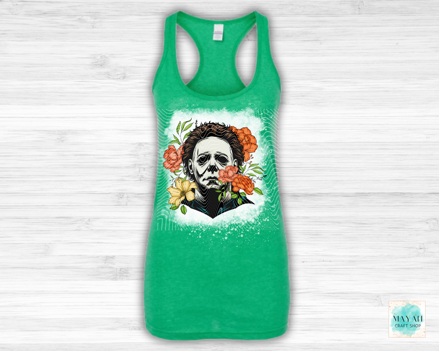 Green tank top with a graphic design of a face surrounded by flowers on a white wooden background.