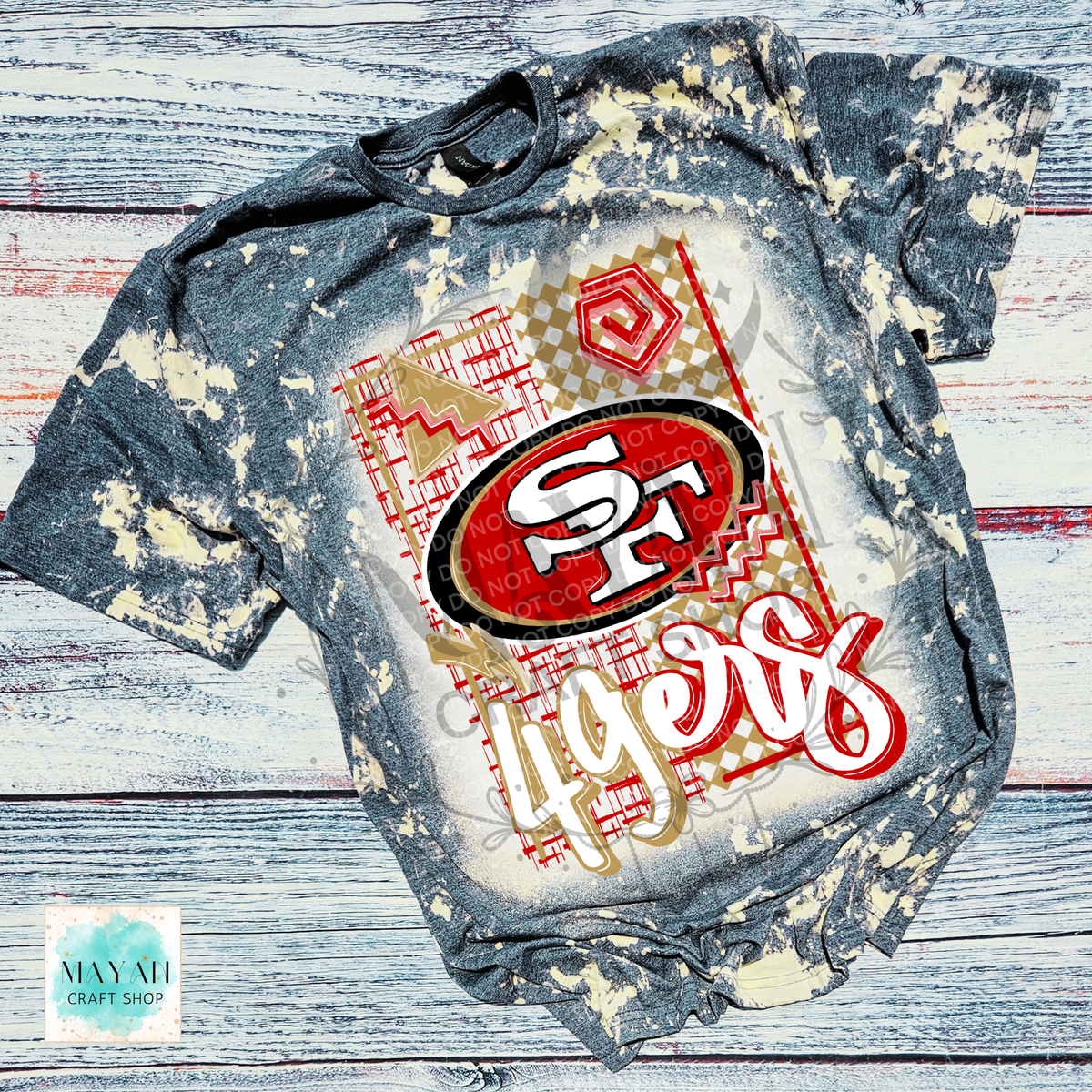 A short-sleeve graphic T-shirt laid flat on a rustic whitewashed wood background. The shirt is bleached on a heather charcoal shirt, with a large front graphic featuring a football team logo.