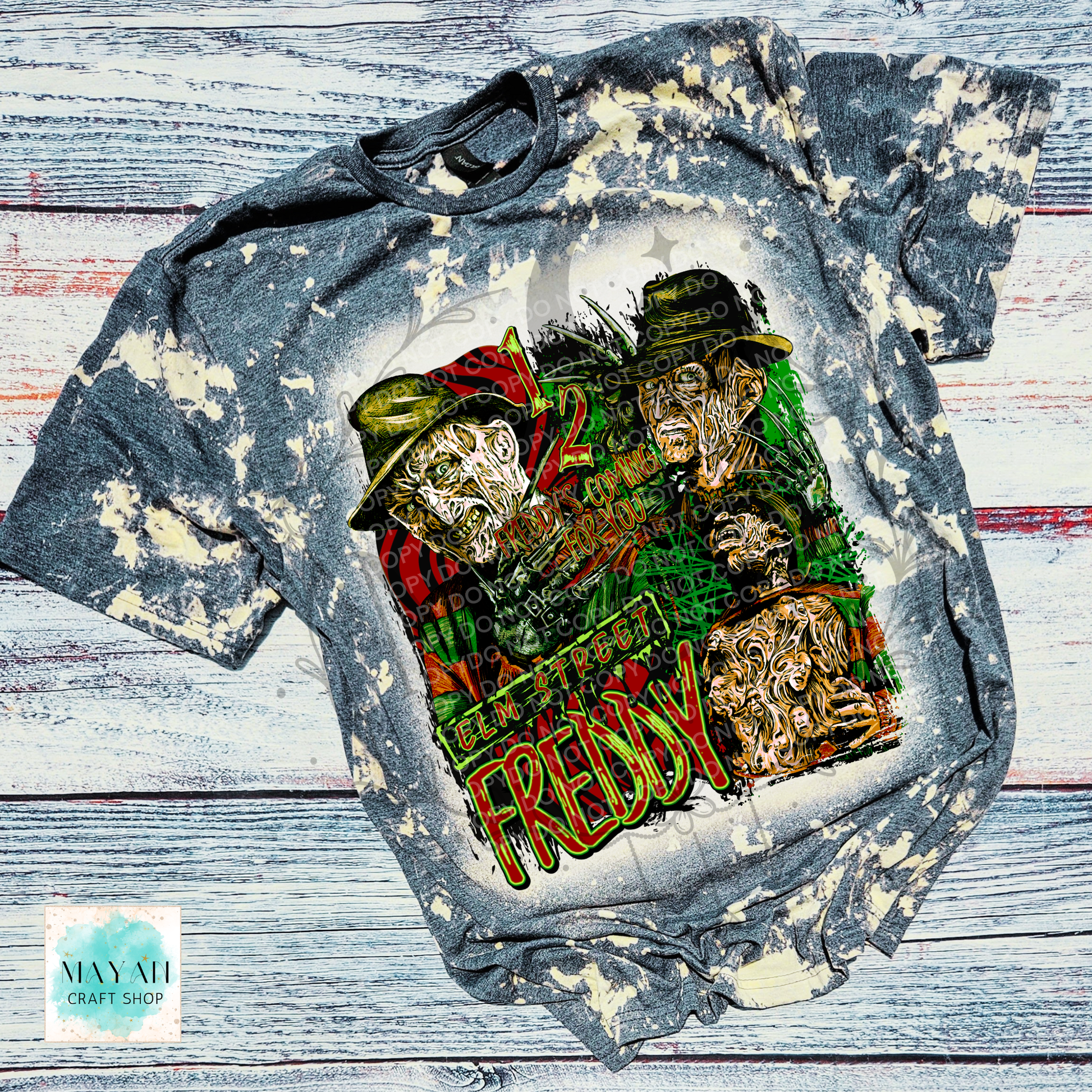 A short-sleeve graphic T-shirt laid flat on a distressed white and gray wood background. The shirt has a bleached, faded gray appearance with a large multicolor horror-themed graphic on the front.