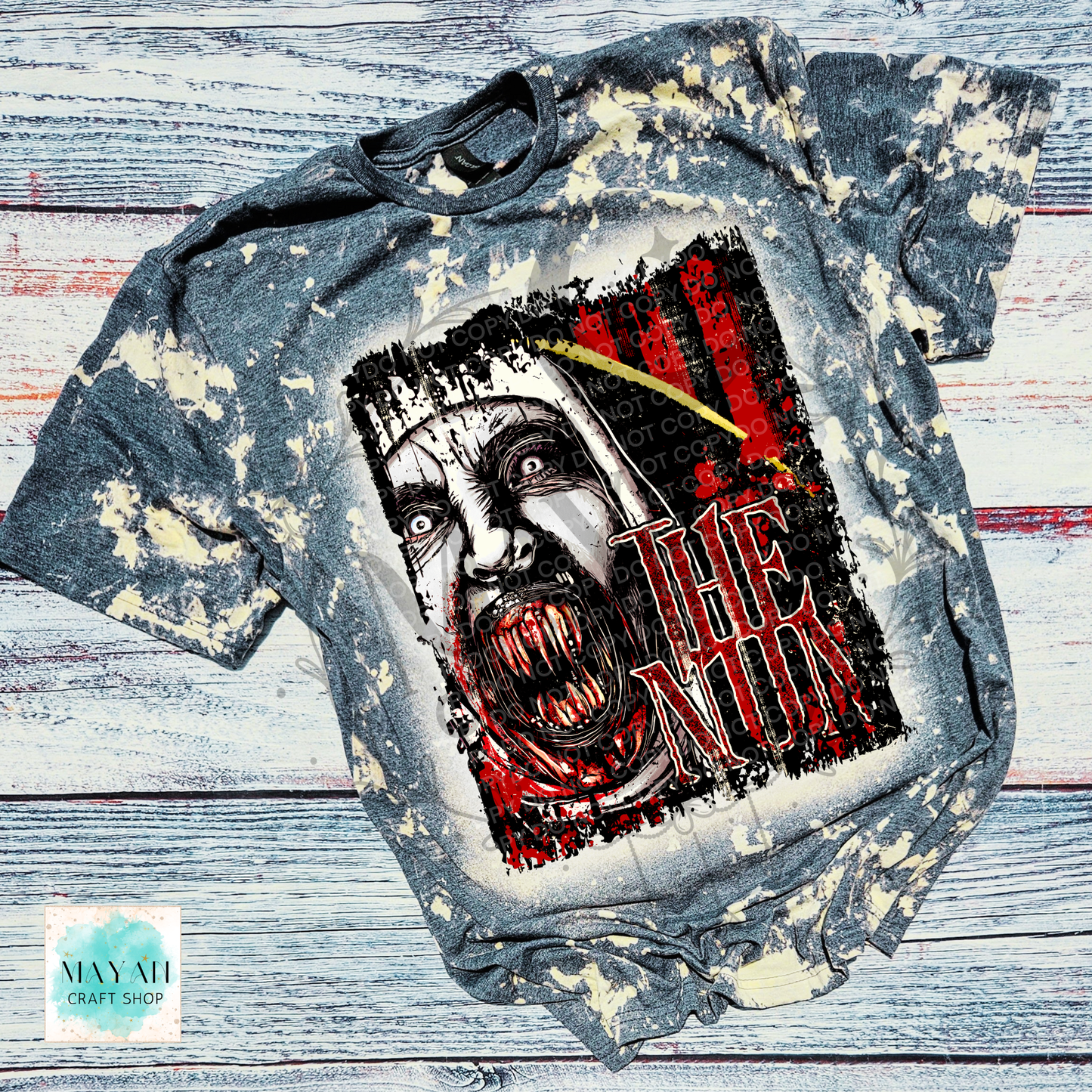 A short-sleeve graphic T-shirt laid flat on a distressed white and gray wood background. The shirt has a bleached, faded gray appearance with cream splatter effects.