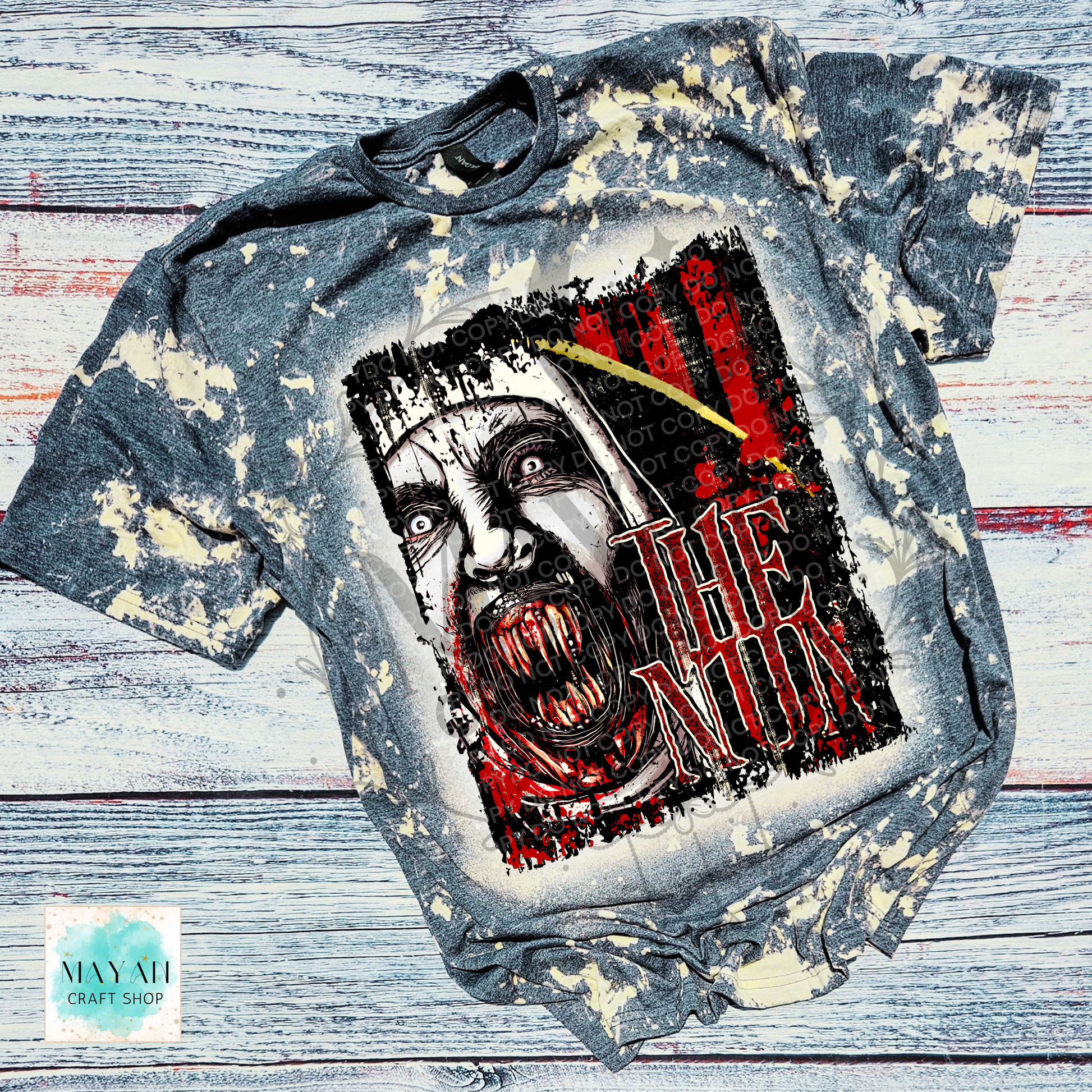 A short-sleeve graphic T-shirt laid flat on a distressed white and gray wood background. The shirt has a bleached, faded gray appearance with cream splatter effects.