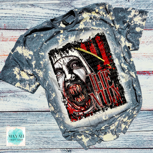 A short-sleeve graphic T-shirt laid flat on a distressed white and gray wood background. The shirt has a bleached, faded gray appearance with cream splatter effects.