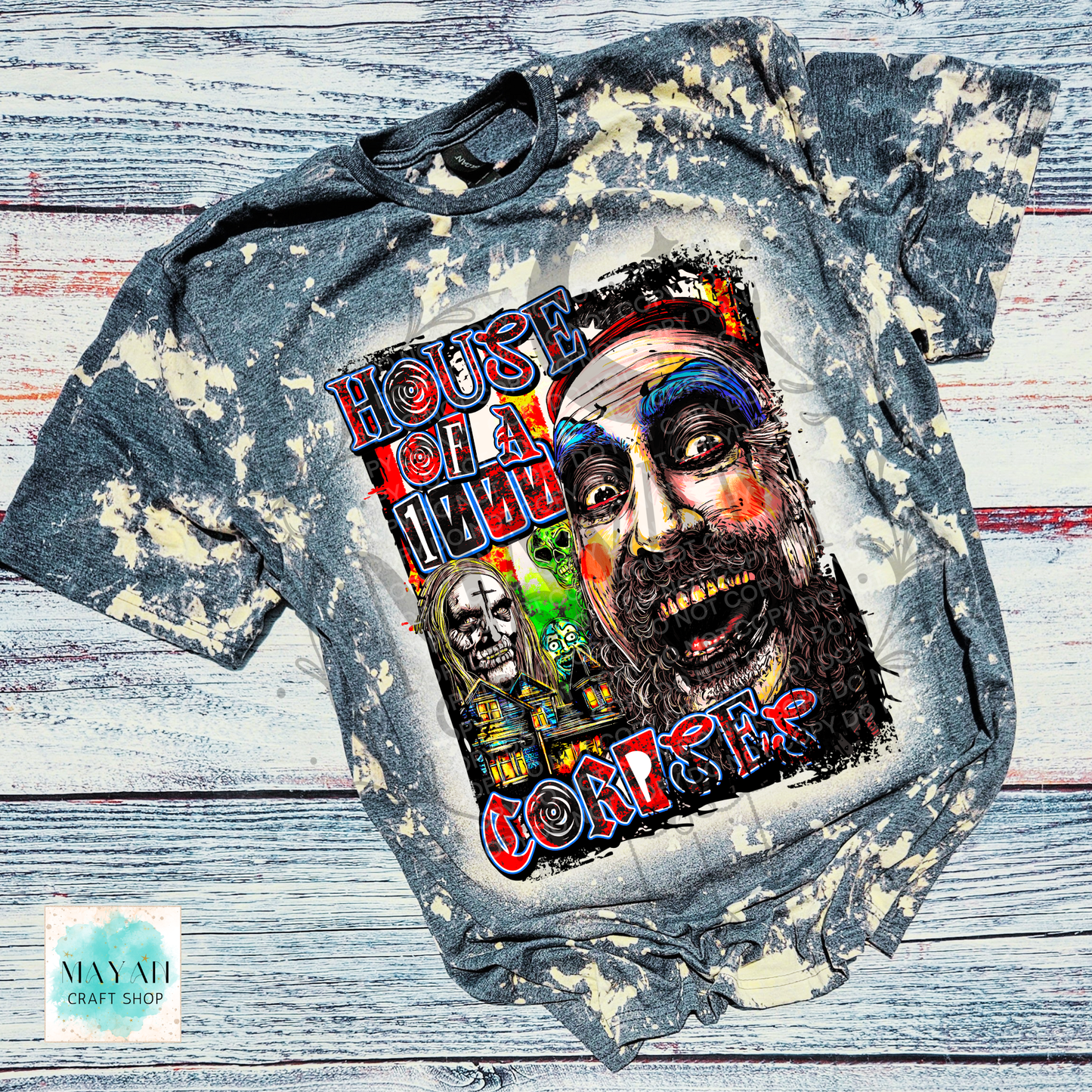 A distressed, bleach-splattered gray t-shirt featuring a large graphic print of a creepy clown face and a text. The shirt is laid flat on a rustic, whitewashed wooden plank background.