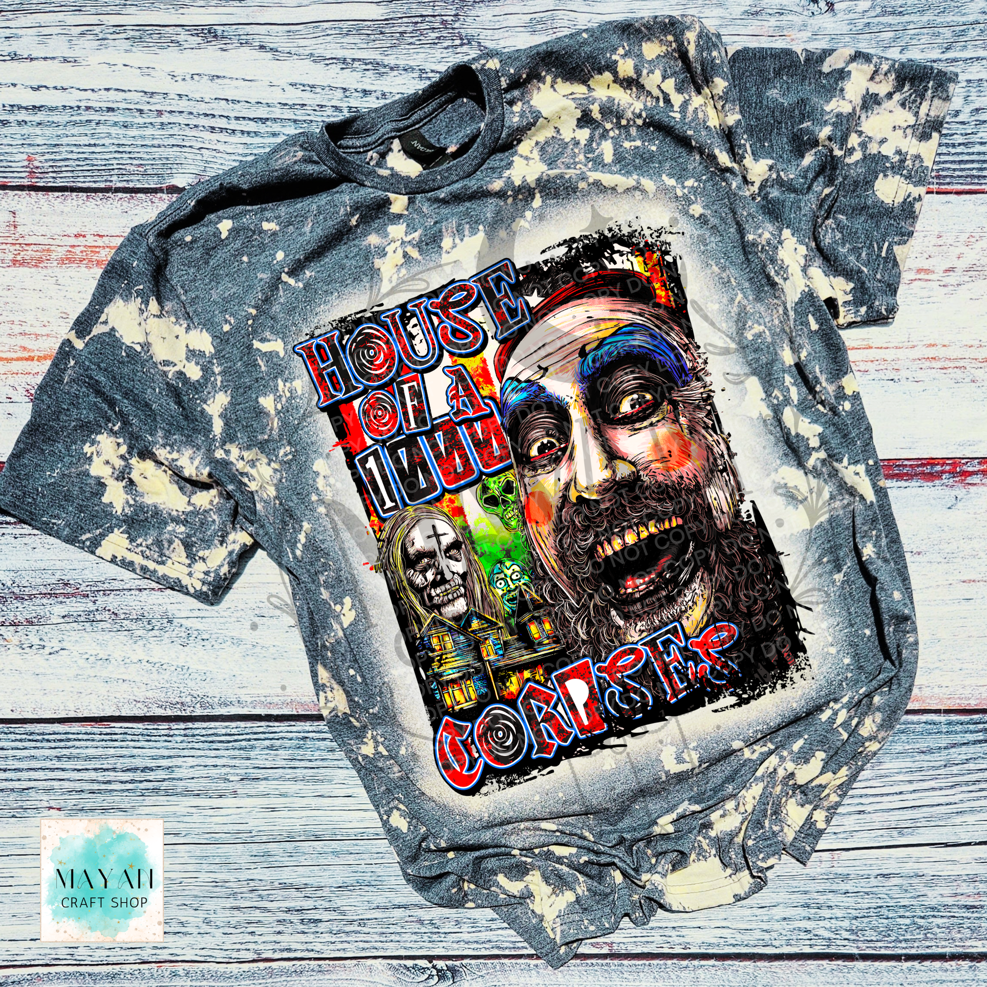 A distressed, bleach-splattered gray t-shirt featuring a large graphic print of a creepy clown face and a text. The shirt is laid flat on a rustic, whitewashed wooden plank background.