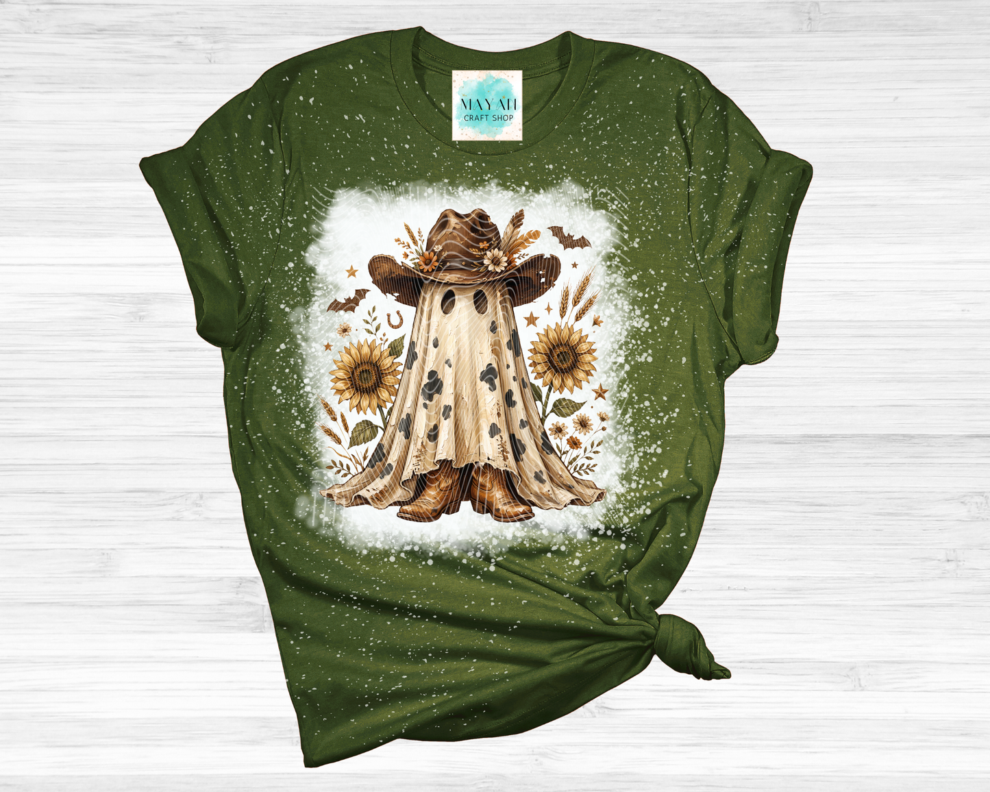 A heather forest green short-sleeve t-shirt with a distressed splatter finish, featuring a central graphic of a ghostly figure in a cowboy hat surrounded by sunflowers, laid flat on a white wood background.