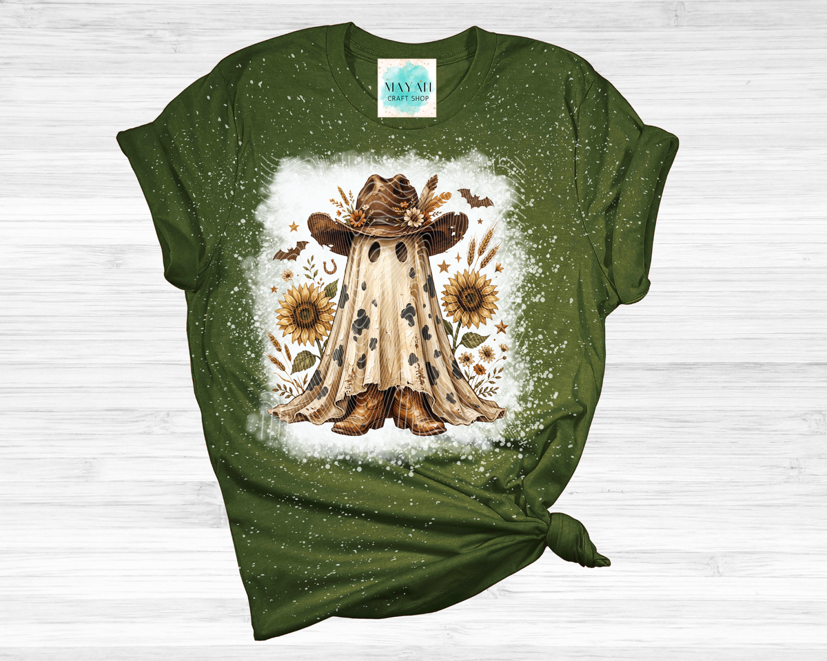 A heather forest green short-sleeve t-shirt with a distressed splatter finish, featuring a central graphic of a ghostly figure in a cowboy hat surrounded by sunflowers, laid flat on a white wood background.