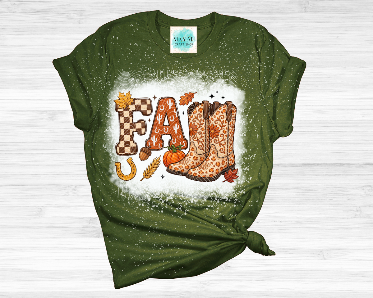 A heather forest green short-sleeve t-shirt with a distressed, splattered finish, styled with a knot at the bottom right. The shirt features a graphic spelling 'FALL' in autumn-themed fonts.