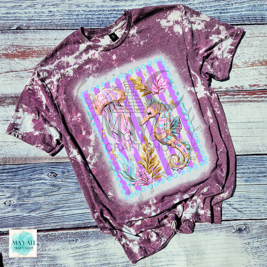 Bleached maroon t-shirt with a colorful seahorse design on a wooden surface