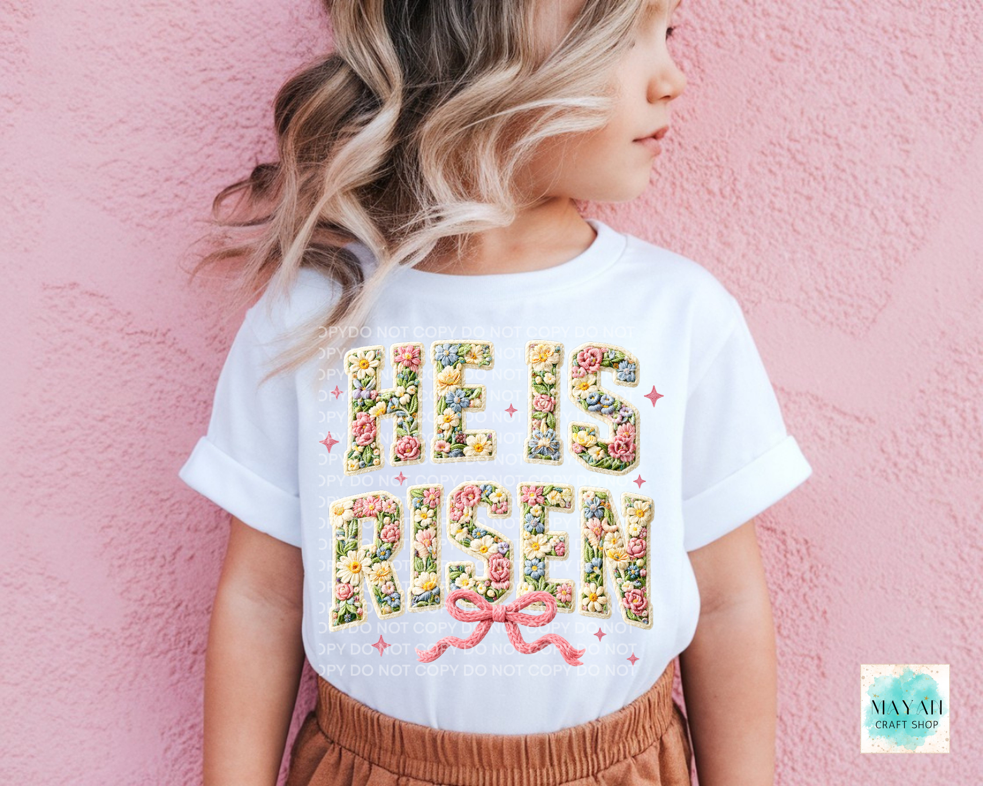 Child wearing a white t-shirt with 'He is Risen' design against a pink background