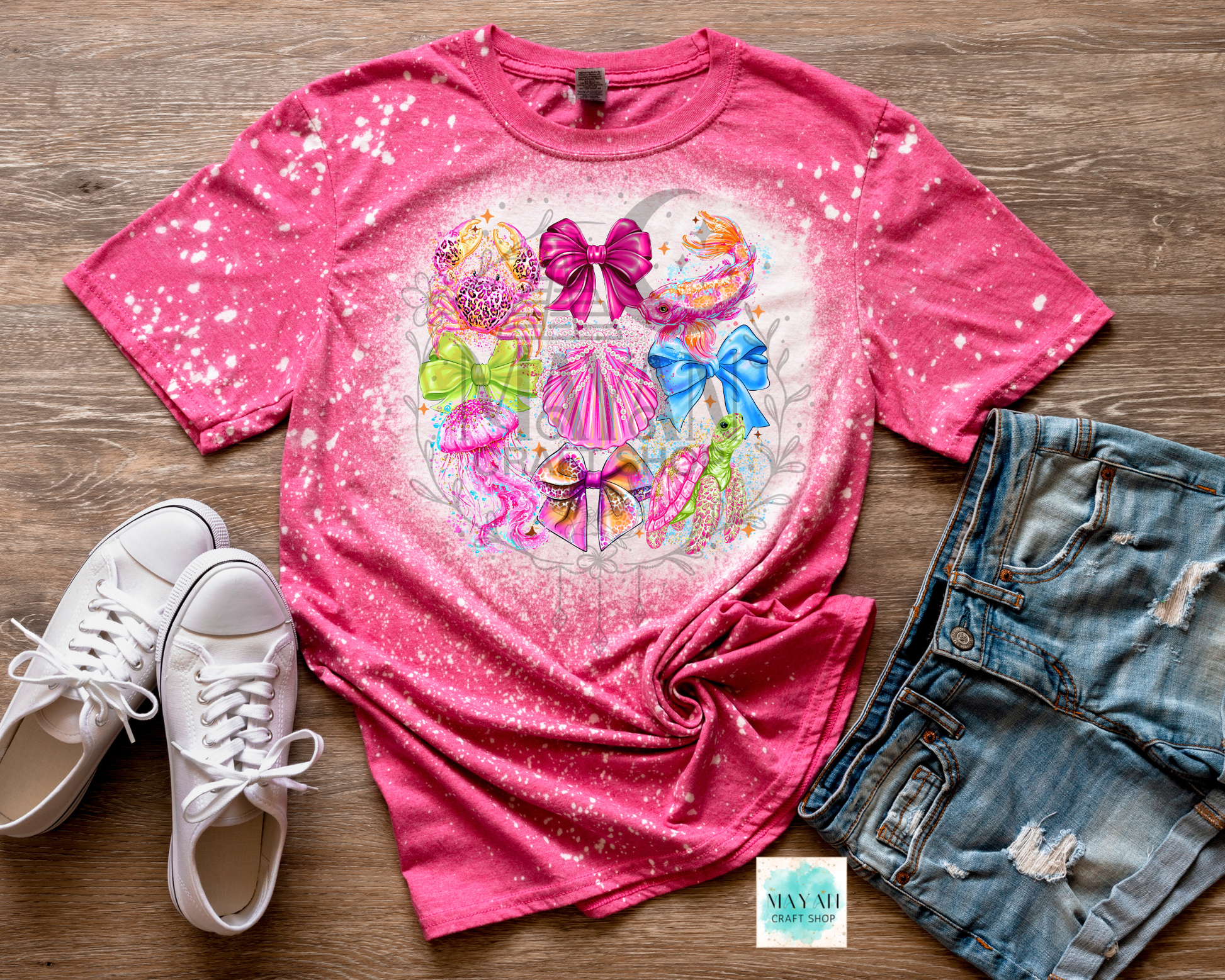 Pink t-shirt with colorful graphic design, white sneakers, and denim shorts on a wooden surface.