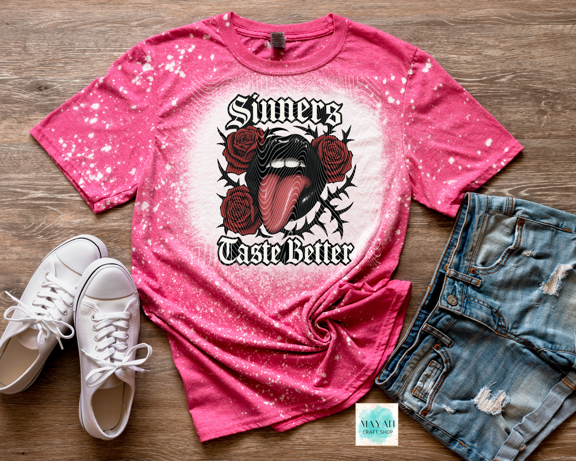 Pink t-shirt with graphic design and text, paired with white sneakers and denim shorts on a wooden surface.
