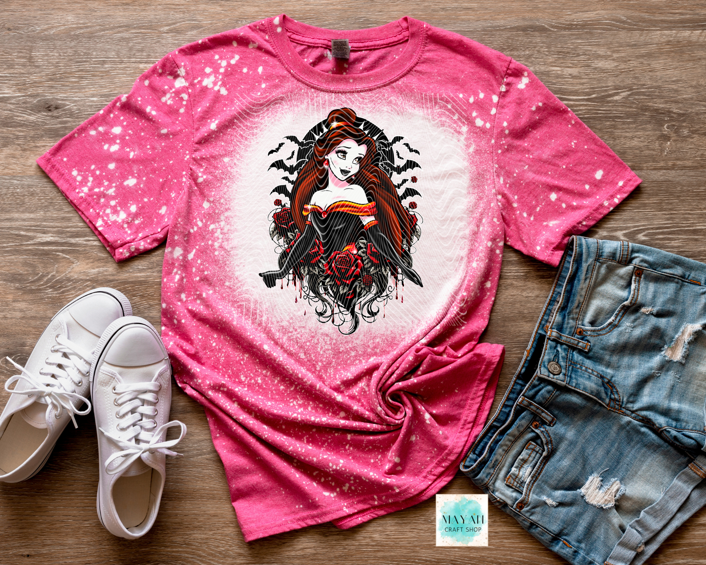 Pink t-shirt with graphic design, white sneakers, and denim shorts on a wooden surface