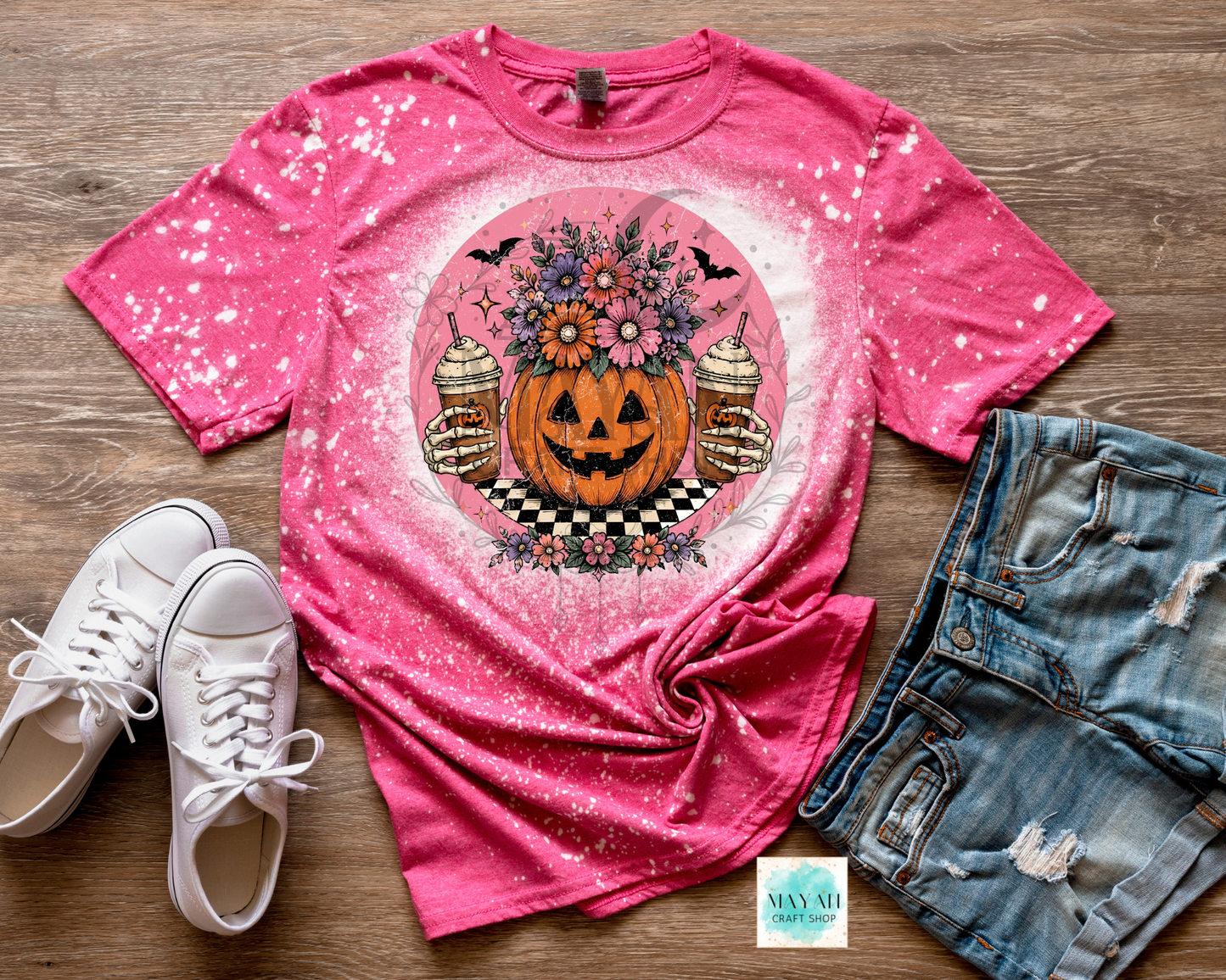 Pink t-shirt with Halloween design, white sneakers, and denim shorts on a wooden surface