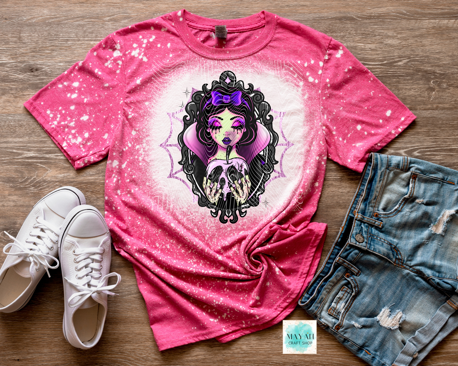 Pink t-shirt with graphic design, white sneakers, and denim shorts on a wooden surface