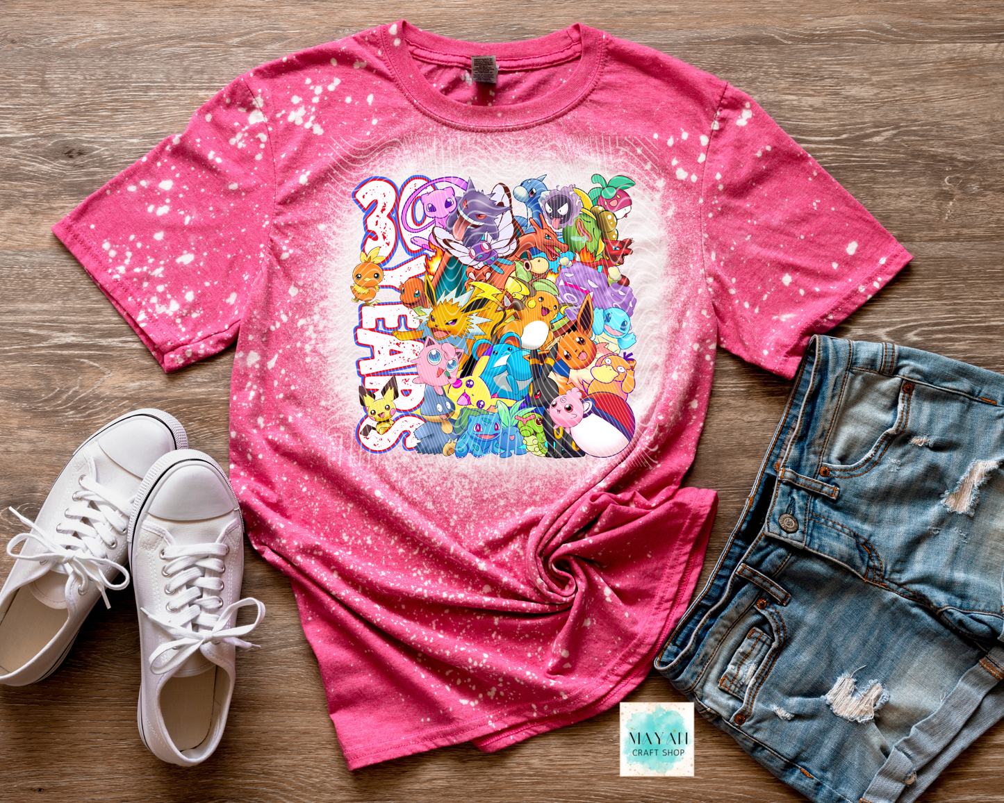 Pink t-shirt with colorful graphic design, white sneakers, and denim shorts on a wooden surface.