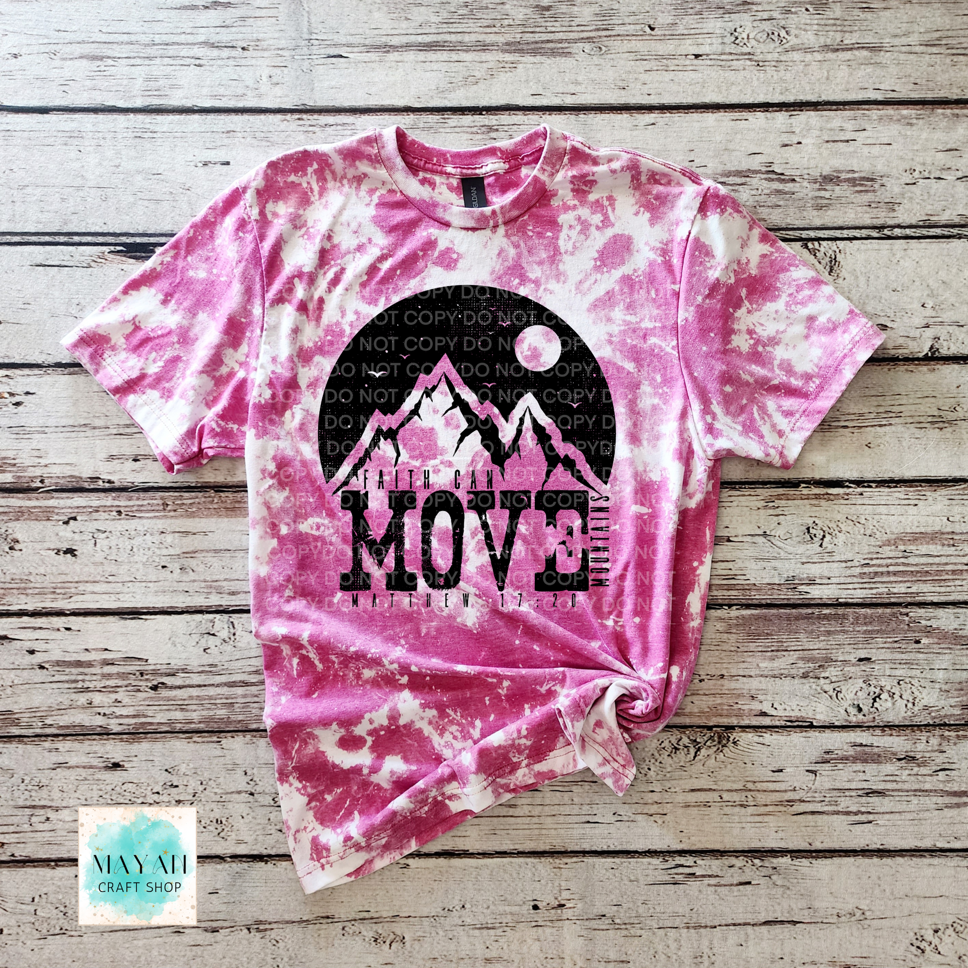 Pink tie-dye t-shirt with mountain design and 'Move Mountains' text on a wooden surface.