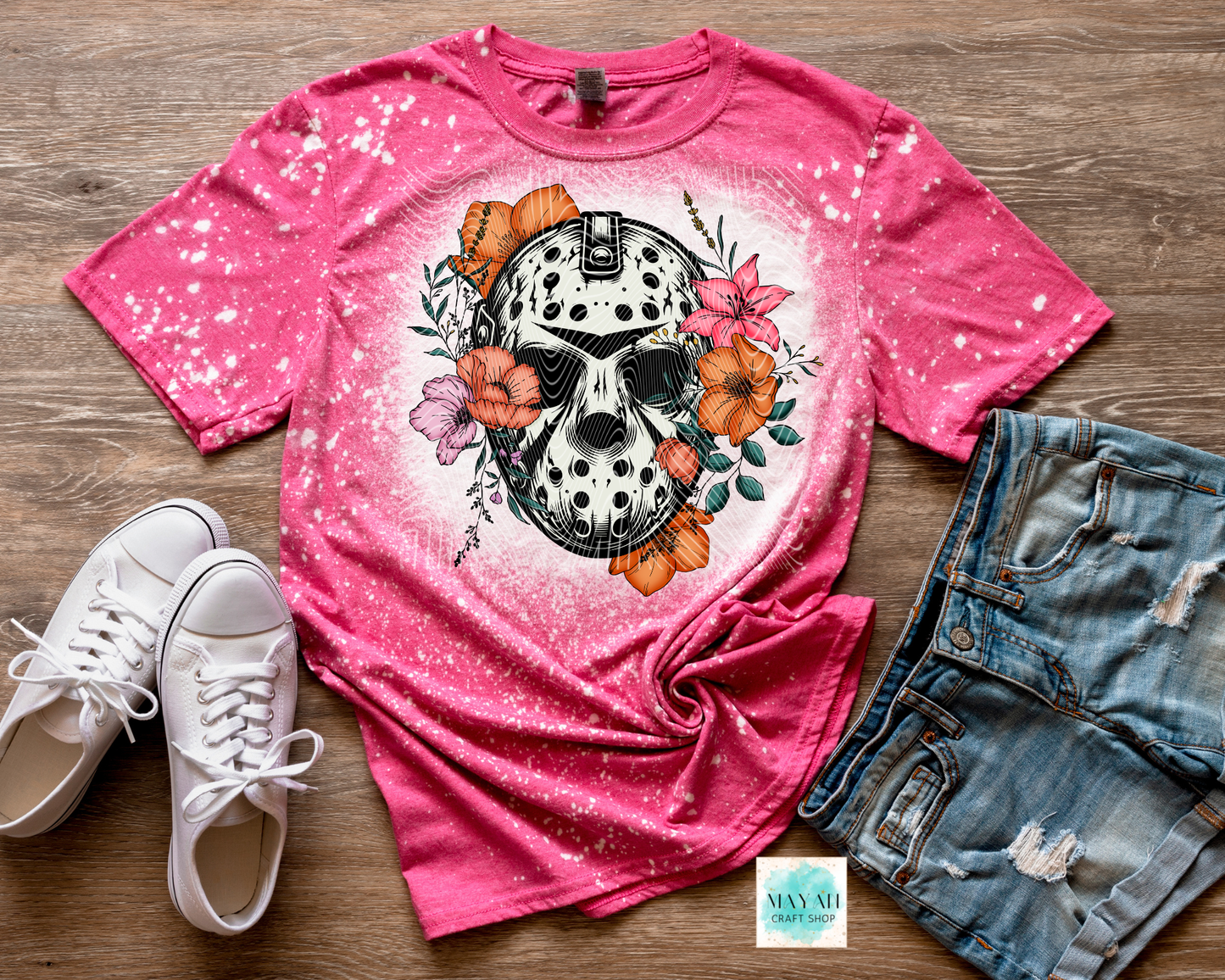 Pink t-shirt with skull and floral design, paired with white sneakers and denim shorts on a wooden surface.