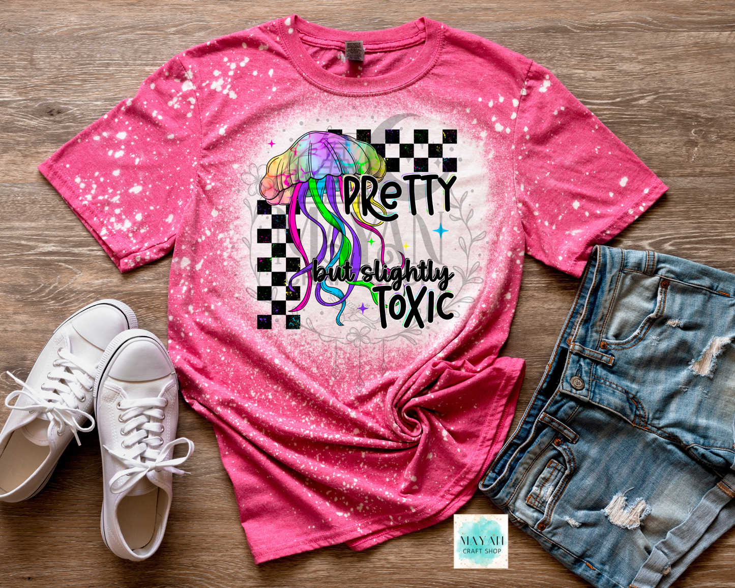Pink t-shirt with colorful jellyfish design and text, paired with white sneakers and denim shorts on a wooden surface.