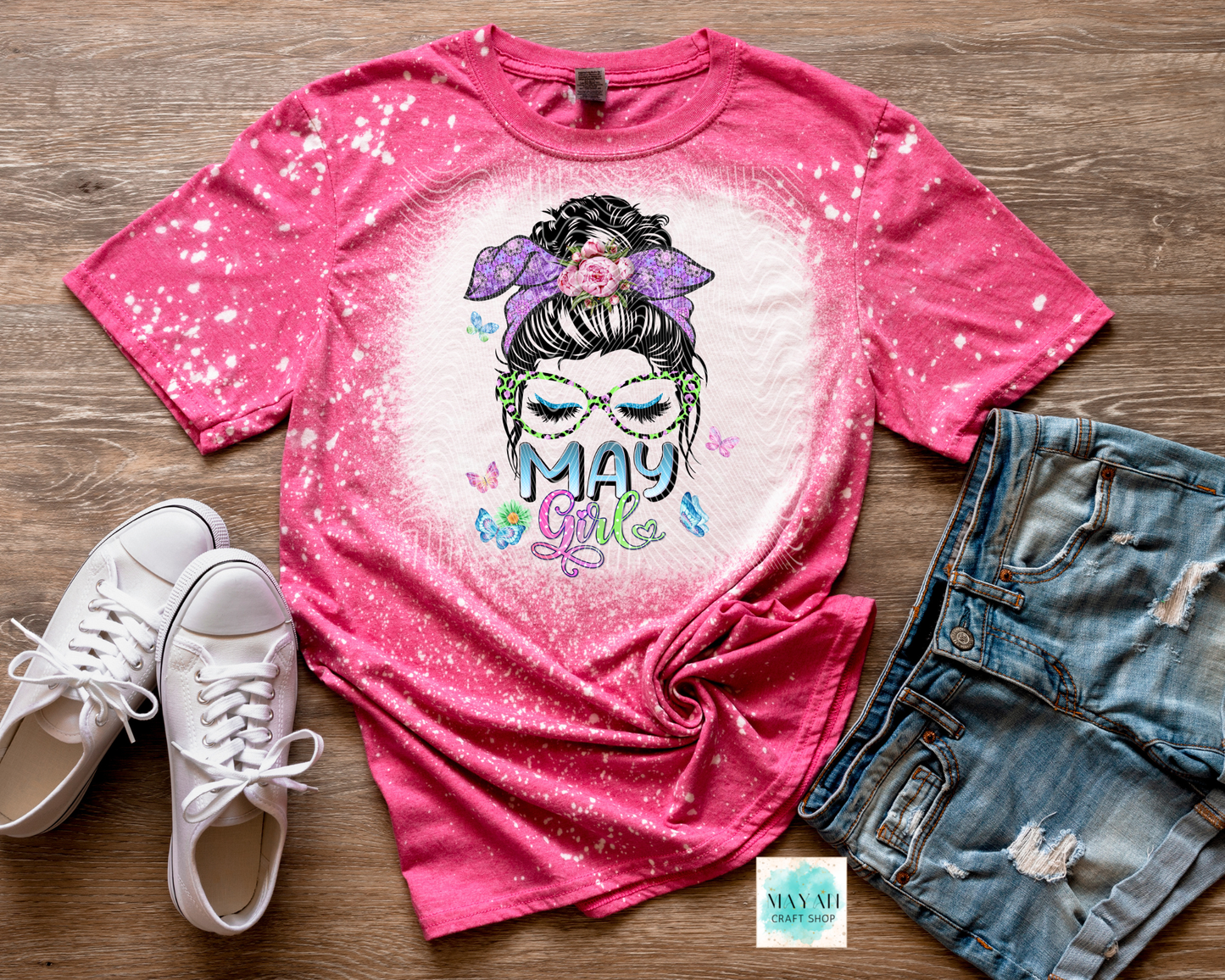 Pink t-shirt with graphic design and text, paired with white sneakers and denim shorts on a wooden surface.