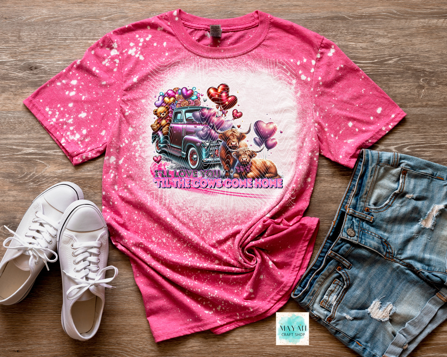 Pink t-shirt with graphic design, white sneakers, and denim shorts on a wooden surface