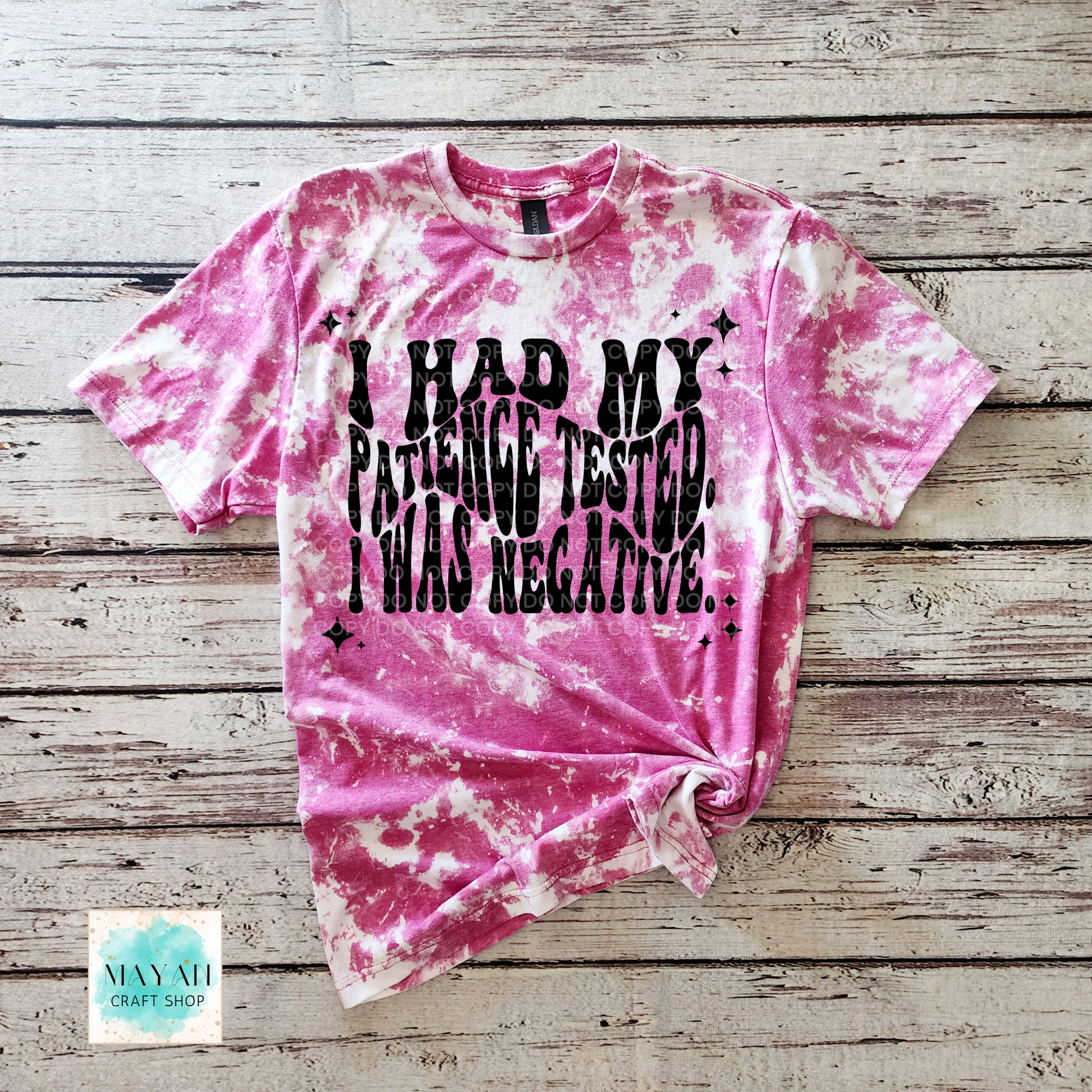 Pink tie-dye t-shirt with black text on a wooden surface, brand 'Mayan Craft Shop'.