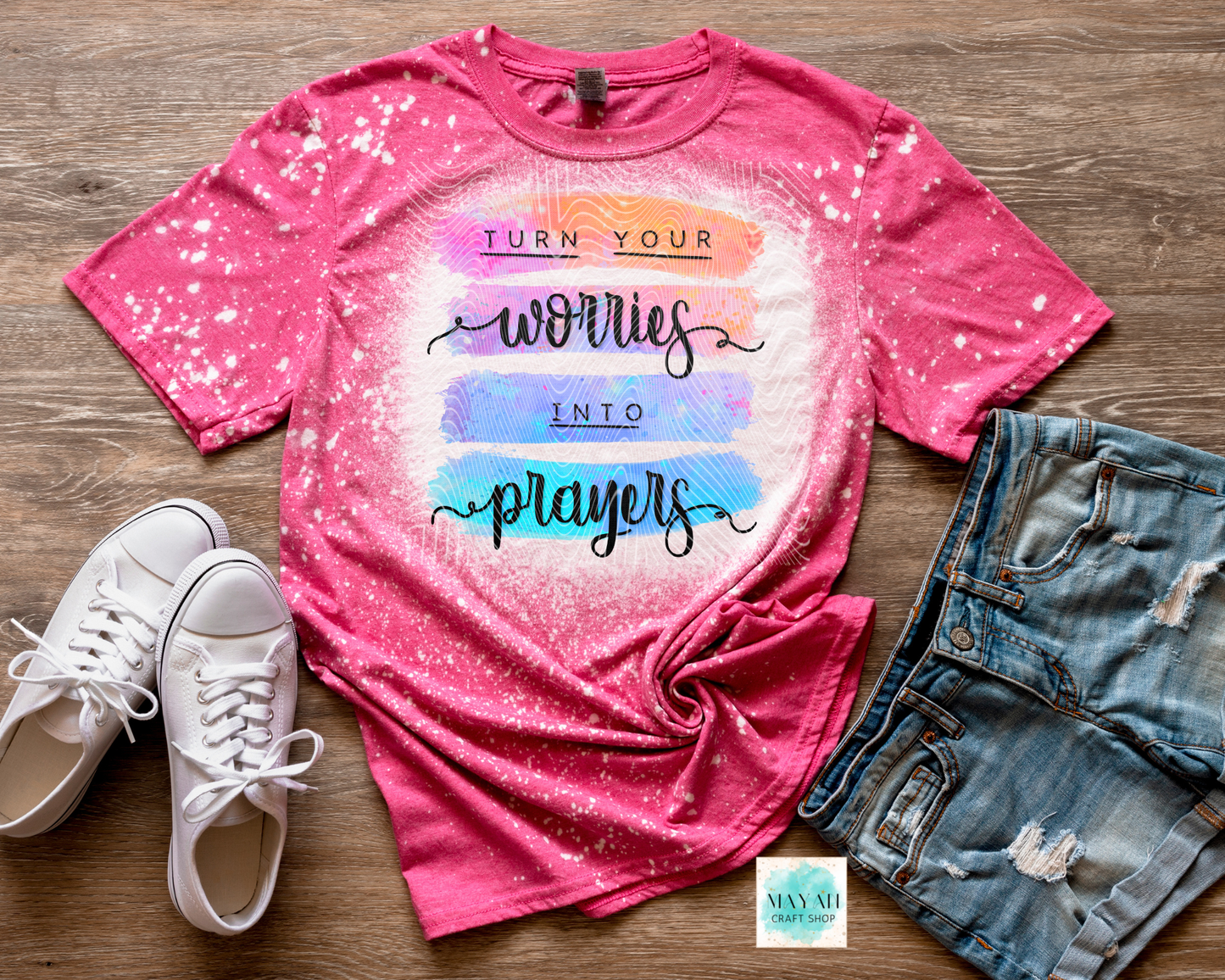 Pink tie-dye t-shirt with motivational quote, white sneakers, and denim shorts on a wooden surface.