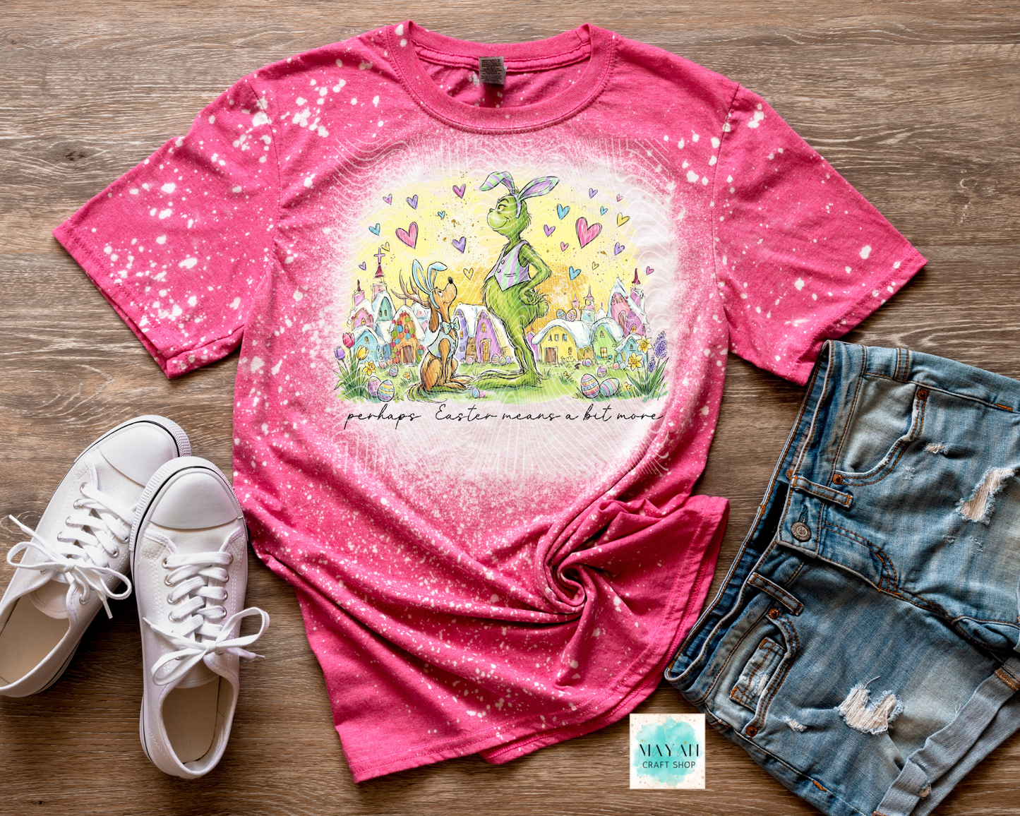 Pink t-shirt with graphic design, white sneakers, and denim shorts on a wooden surface