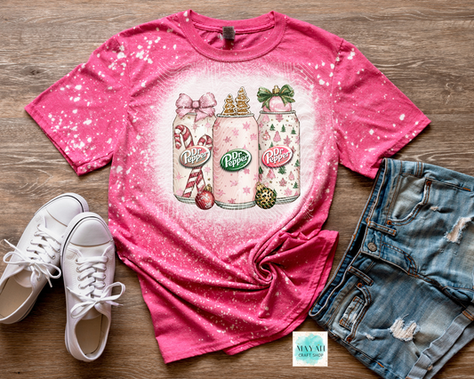 Pink t-shirt with soft drinks design on a wooden surface with white sneakers and denim shorts.