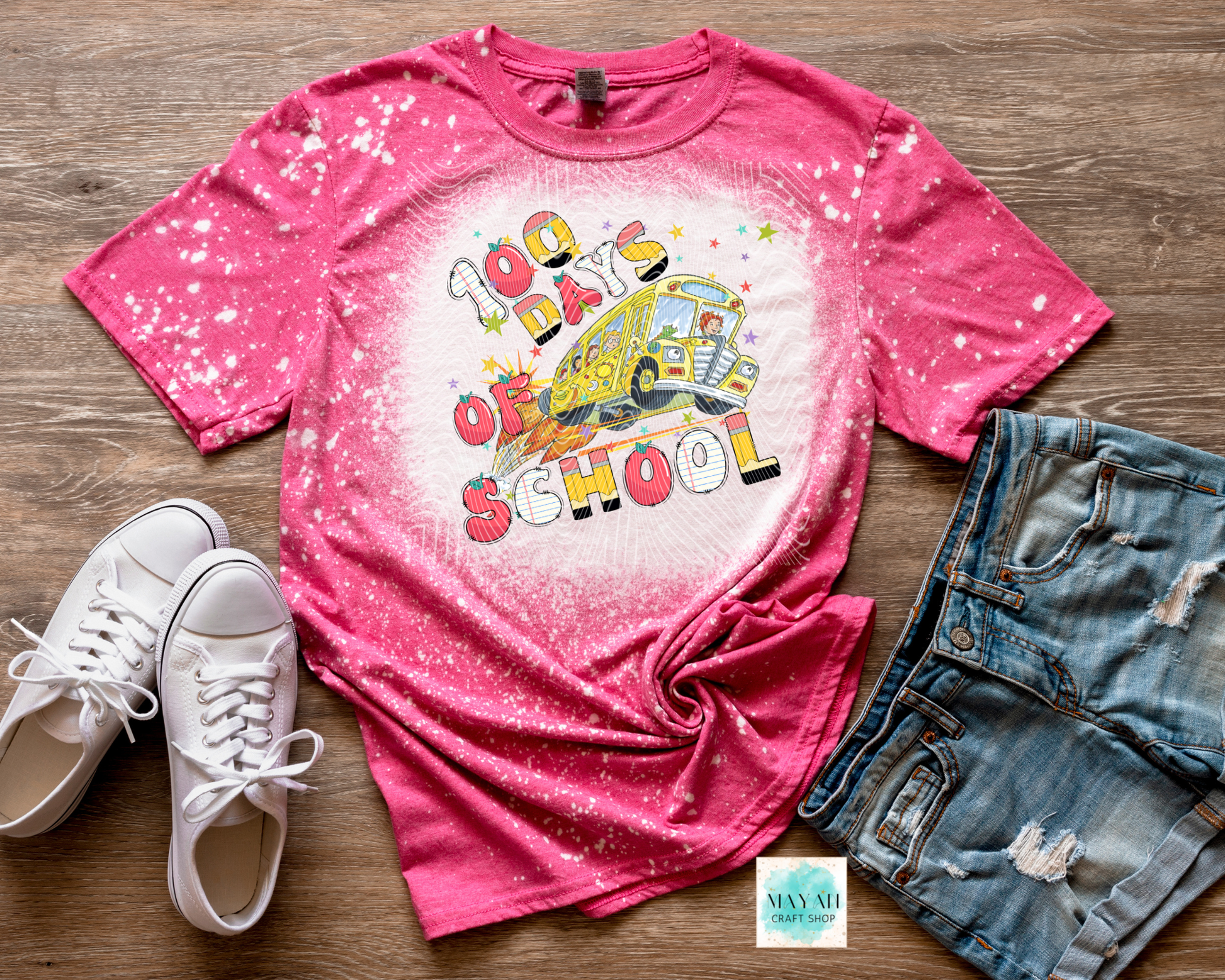 Pink t-shirt with 'Back to School' graphic, white sneakers, and denim shorts on a wooden surface.
