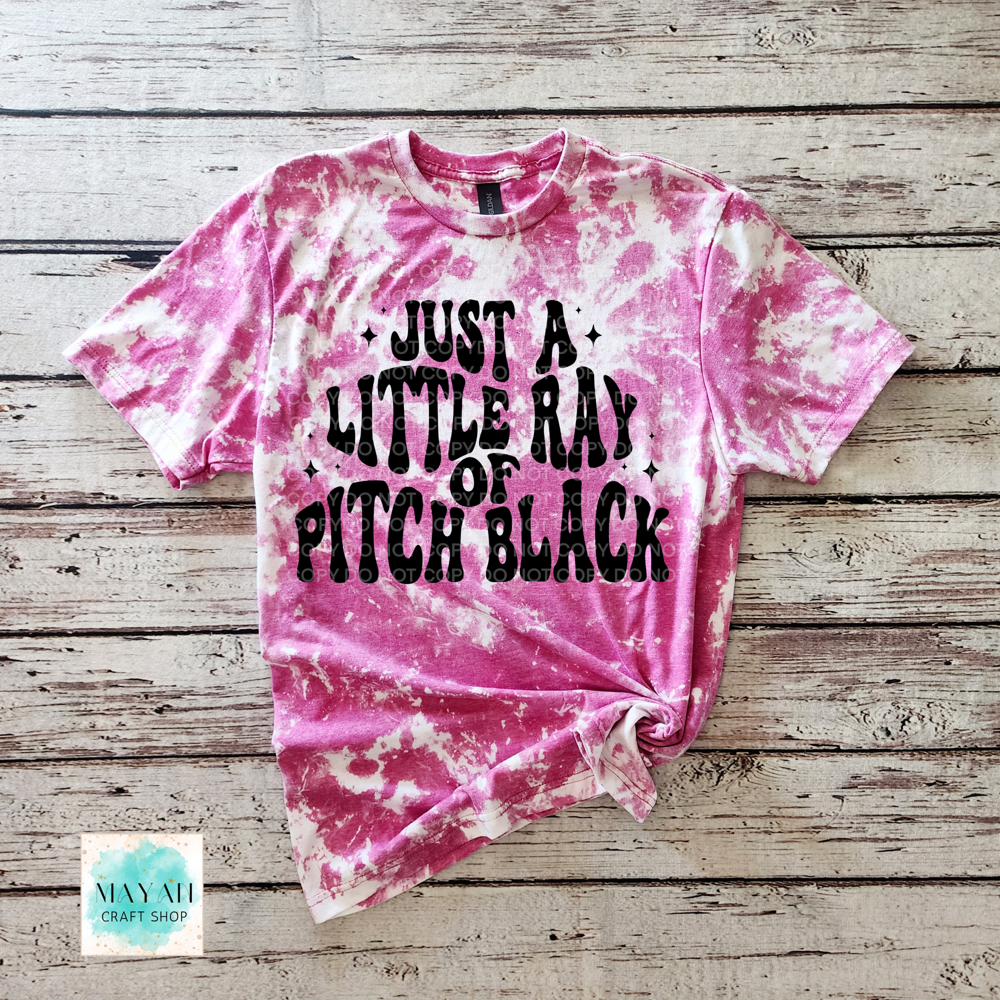 Pink tie-dye t-shirt with text on a wooden surface, brand 'Mayan Craft Shop'.
