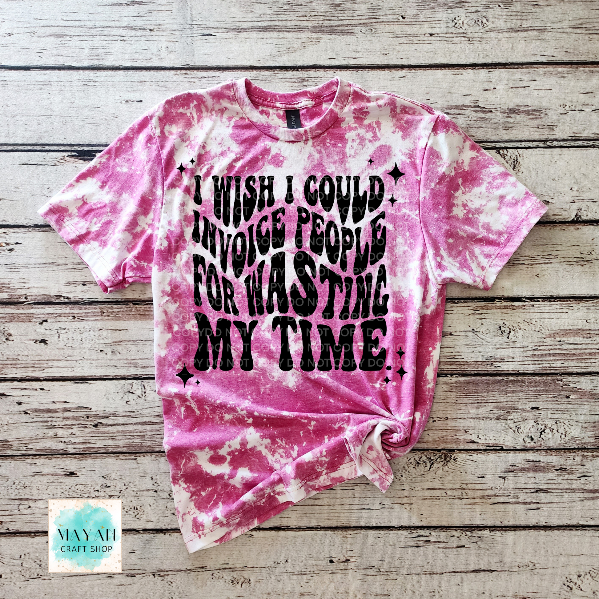 Pink tie-dye t-shirt with black text on a wooden surface, featuring the brand 'Mayan Craft Shop'.