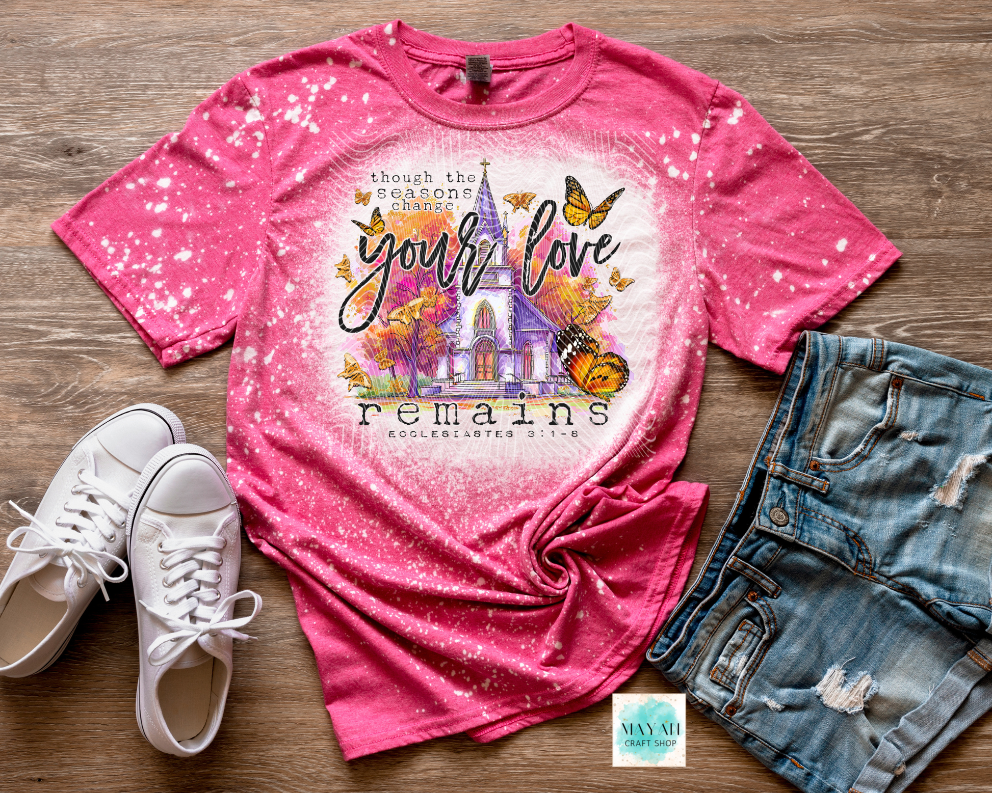 Pink t-shirt with graphic design and text, paired with white sneakers and denim shorts on a wooden surface.