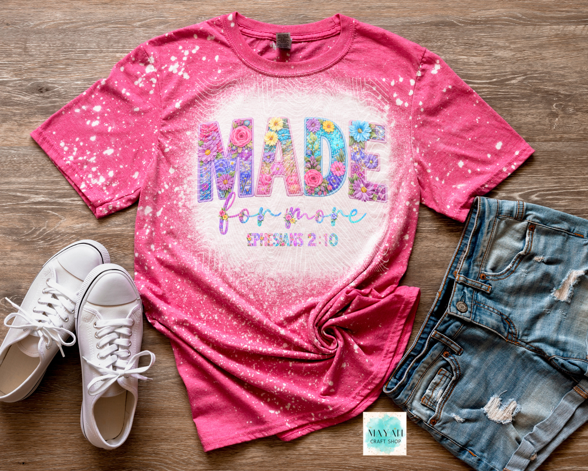 Pink t-shirt with colorful text, white sneakers, and denim shorts on a wooden surface