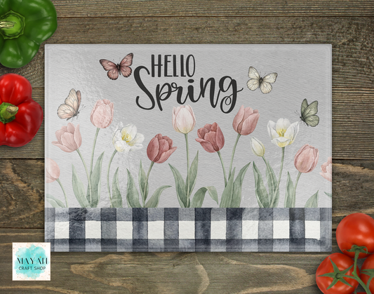 Decorative cutting board with 'Hello Spring' text and floral design on a wooden surface.