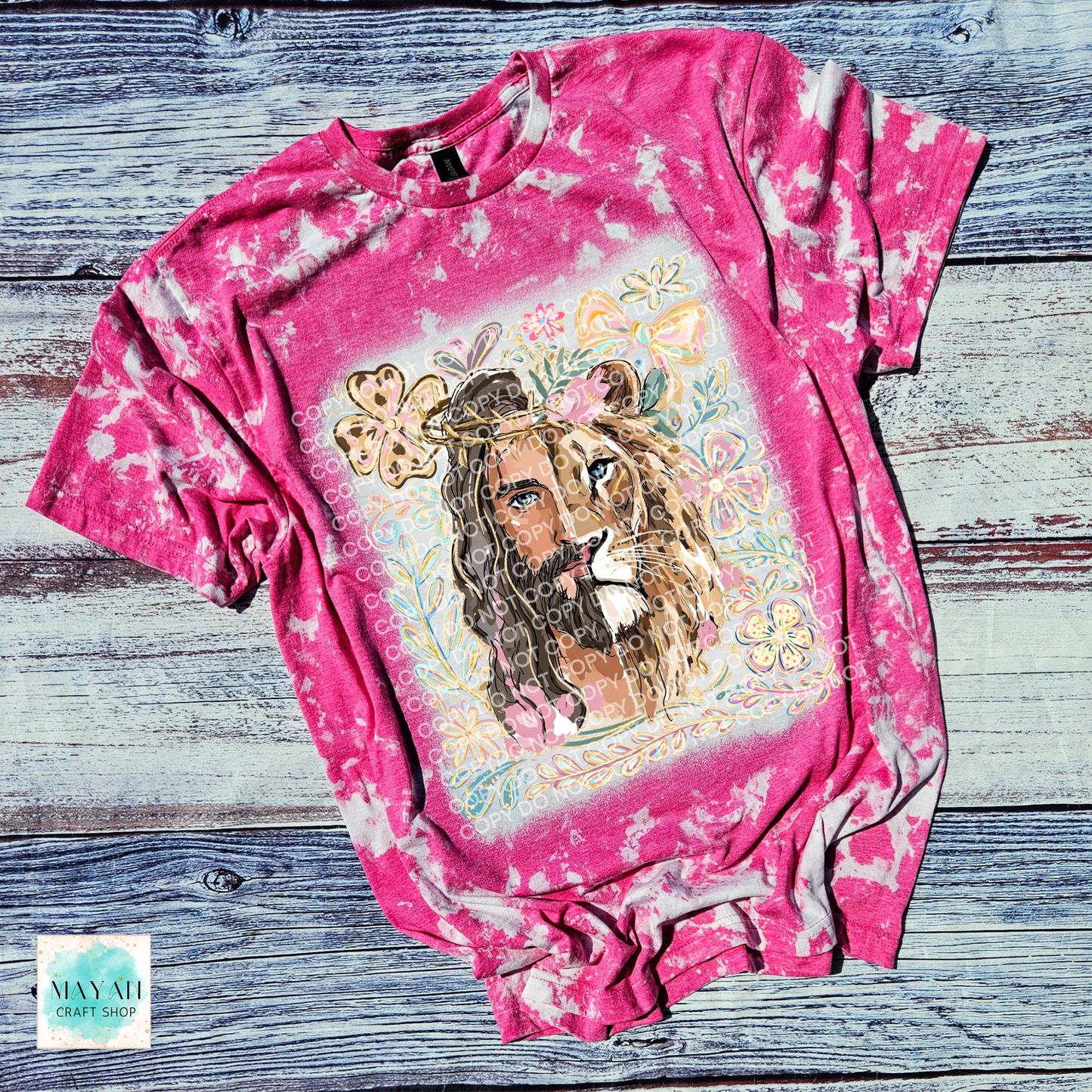 Pink tie-dye t-shirt with a graphic of a lion wearing a crown and flowers on a wooden surface.