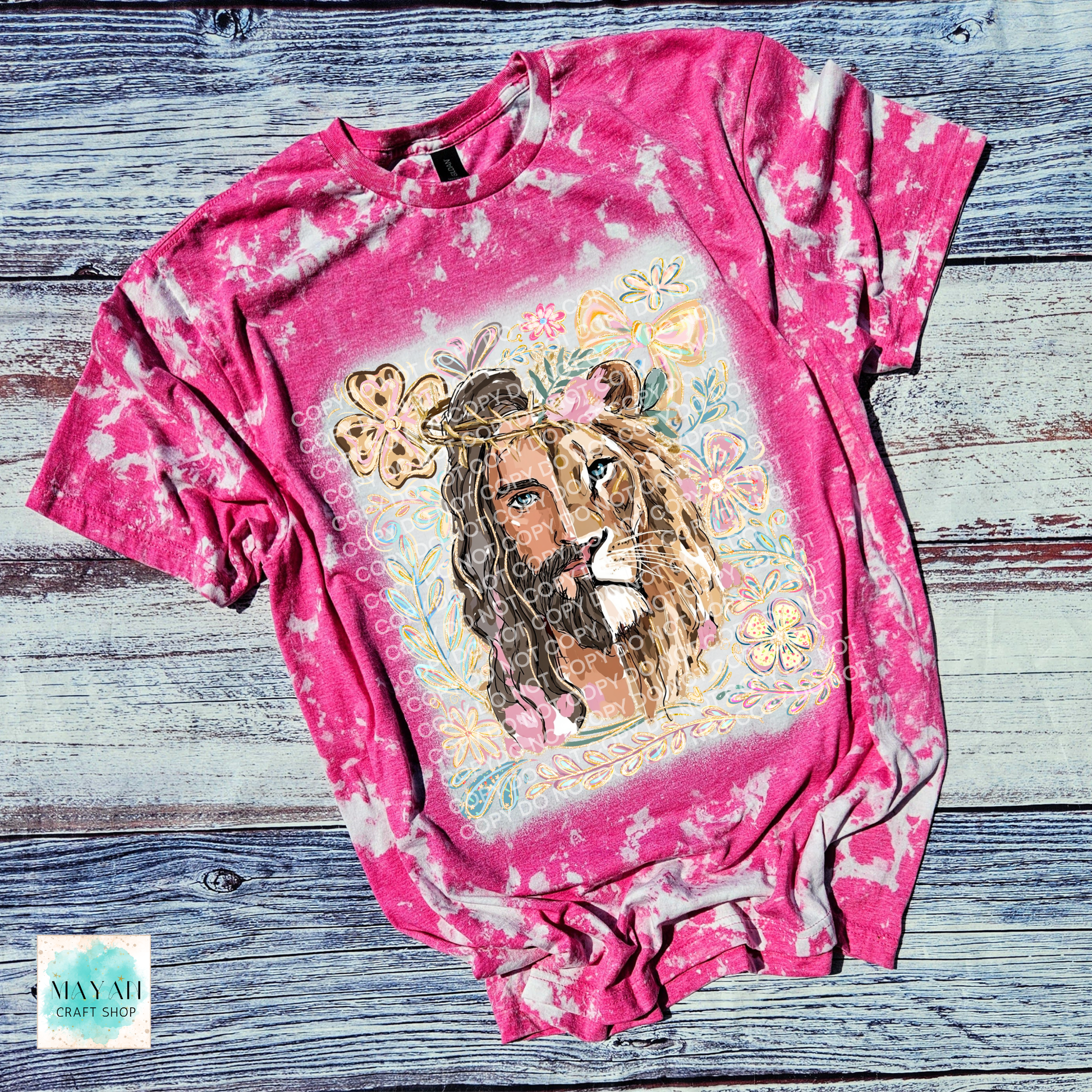 Pink tie-dye t-shirt with a graphic of a lion wearing a crown and flowers on a wooden surface.