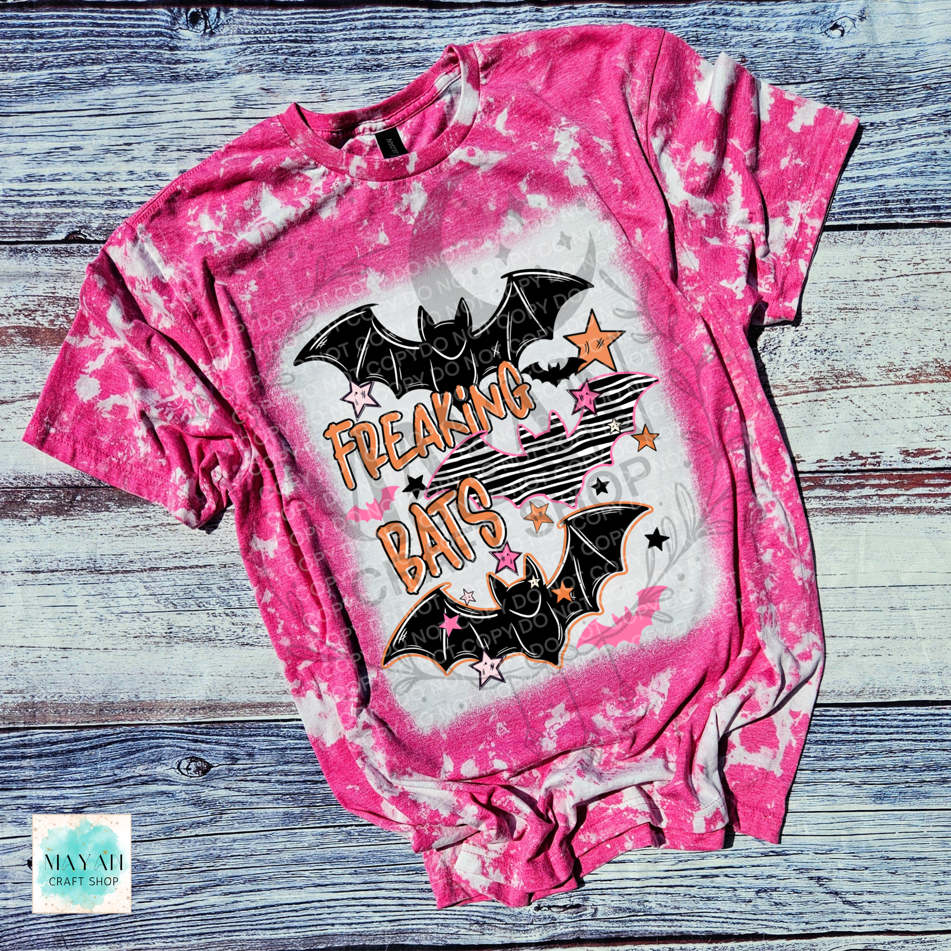 A pink bleached graphic t-shirt featuring two black bats and the words 'FREAKING BATS' in orange, laid flat on a rustic gray wood plank background.