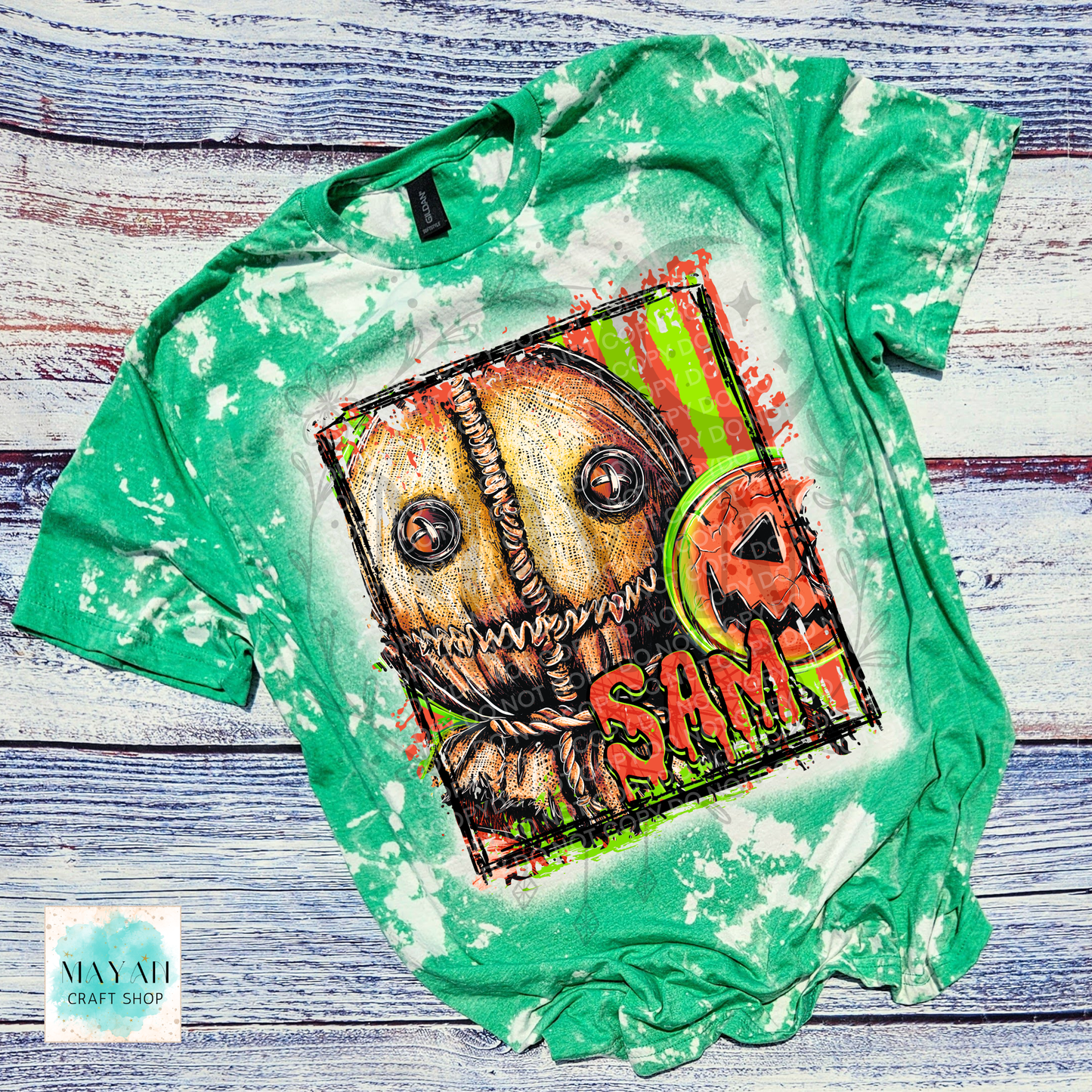 A green bleached graphic t-shirt featuring a horror-themed pumpkin illustration with a word in red, laid flat on a rustic blue-gray wooden background. 