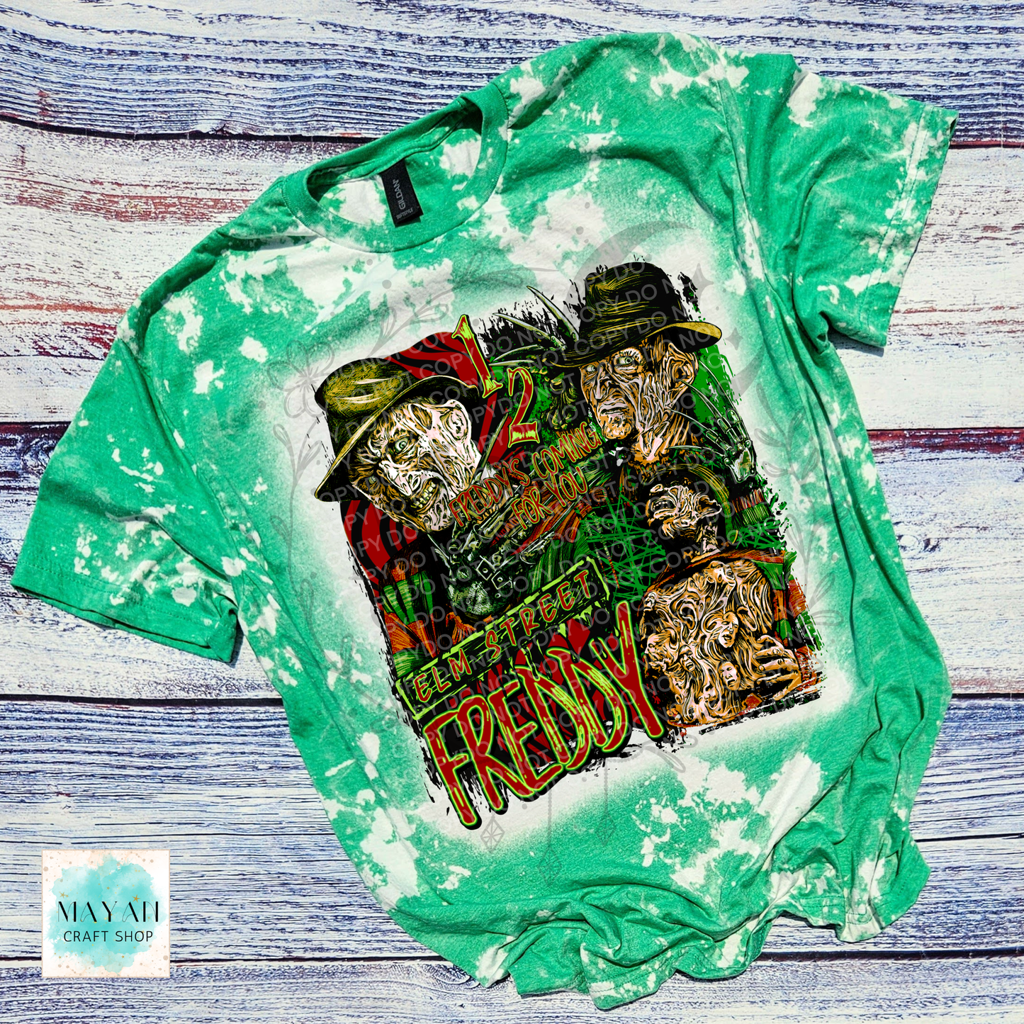A green bleached t-shirt featuring a horror-themed graphic, laid flat on a rustic whitewashed wooden background.