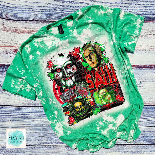 A green bleached t-shirt featuring a large graphic print of characters and title, laid flat on a rustic whitewashed wooden background.