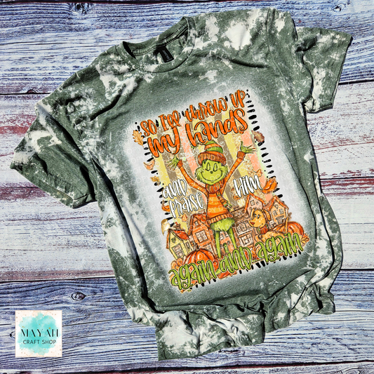 Bleached green t-shirt with a graphic design of a character and text on a wooden surface.