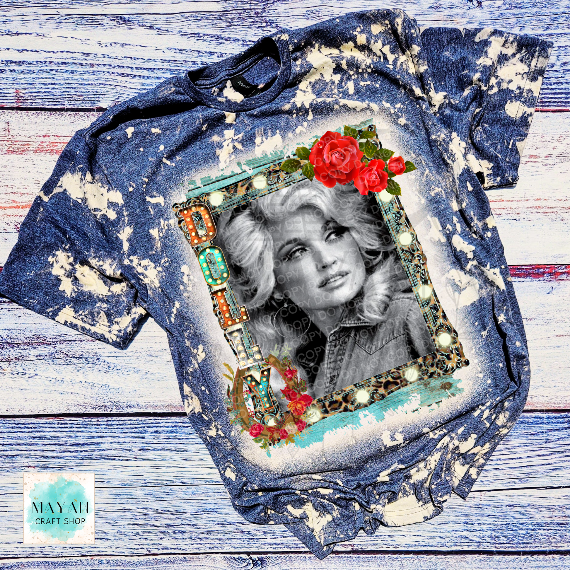 A navy acid-wash graphic t-shirt featuring a portrait of Da country singer inside a decorative frame with red roses, laid flat on a rustic white and blue wooden background.