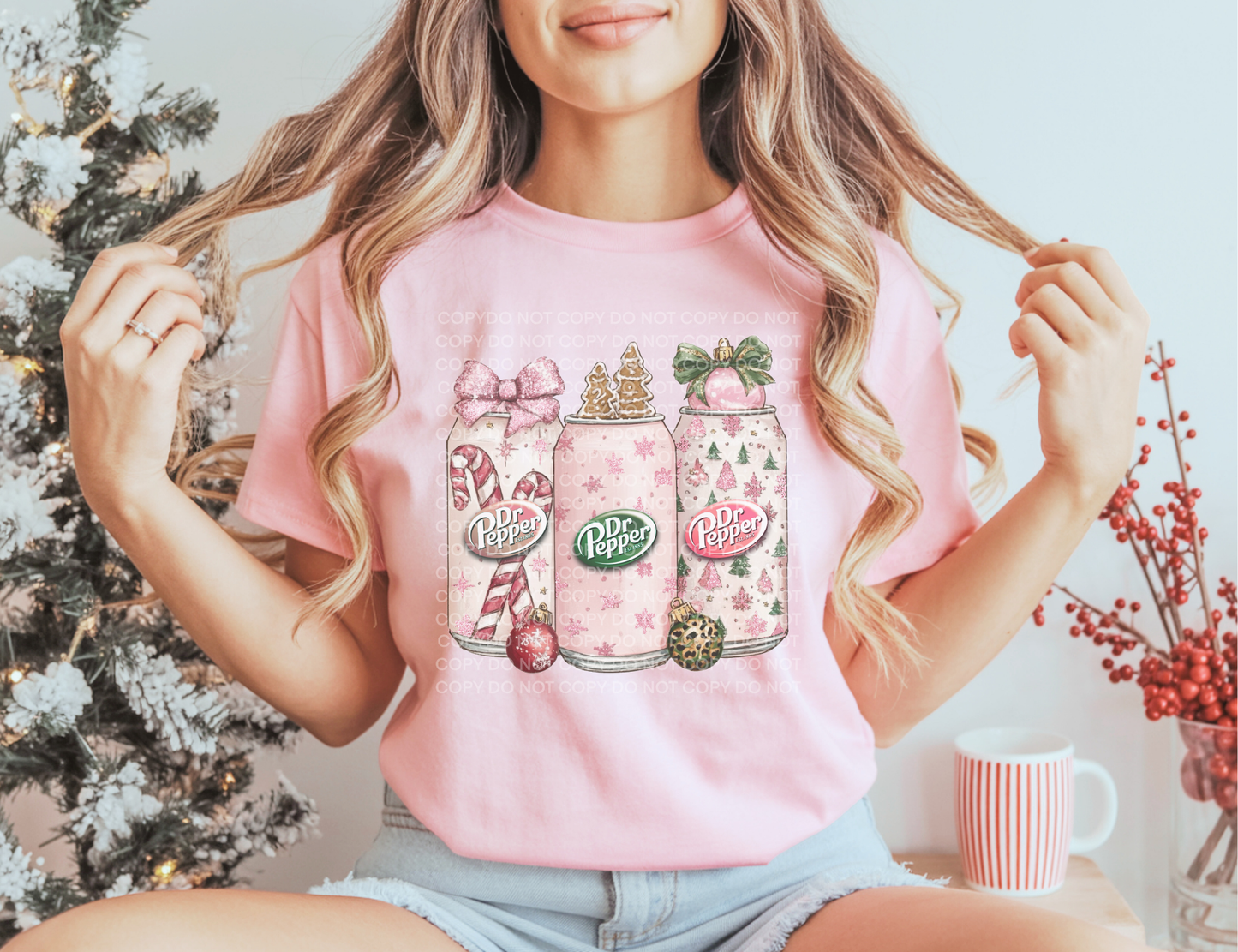Person wearing a pink t-shirt with a design of soft drinks and Christmas elements, sitting in front of a decorated Christmas tree.