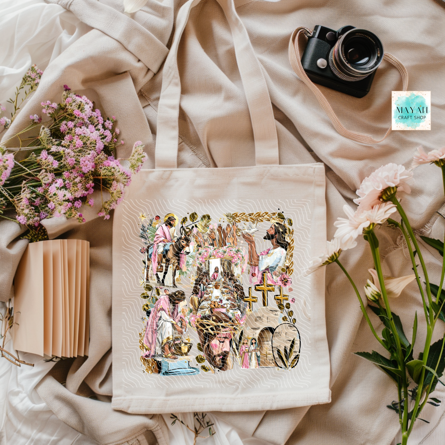 Tote bag with artistic design on a soft fabric background with flowers and a camera.