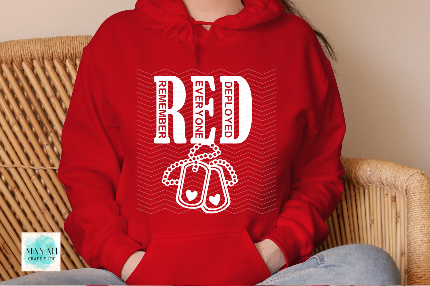 Red hoodie with white text and design, worn by a person sitting on a wicker chair.