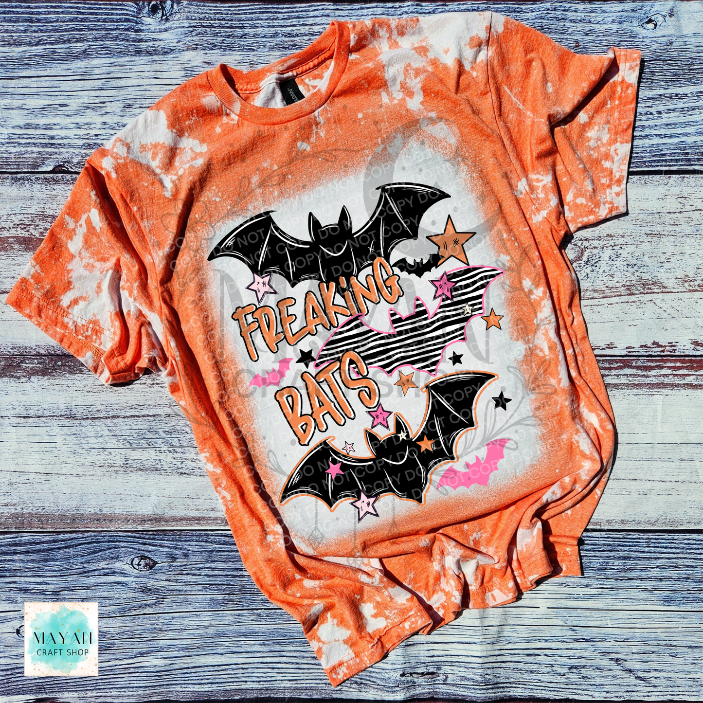 An orange bleached graphic t-shirt featuring two black bats, stars, and the text 'FREAKING BATS' in orange. The shirt is laid flat on a rustic, weathered gray wood plank background.