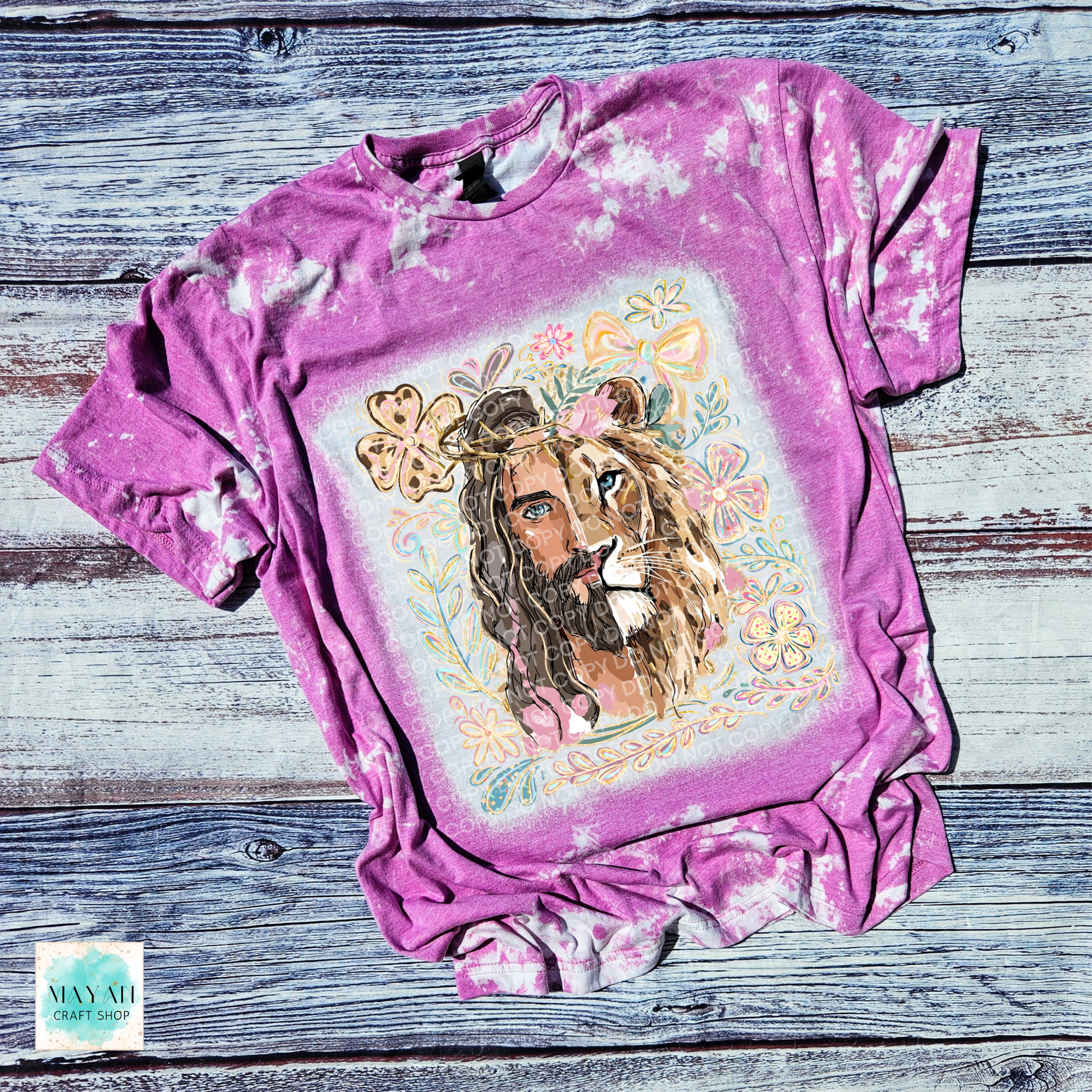 Pink tie-dye t-shirt with a graphic of a woman with a lion's head and flowers on a wooden surface.